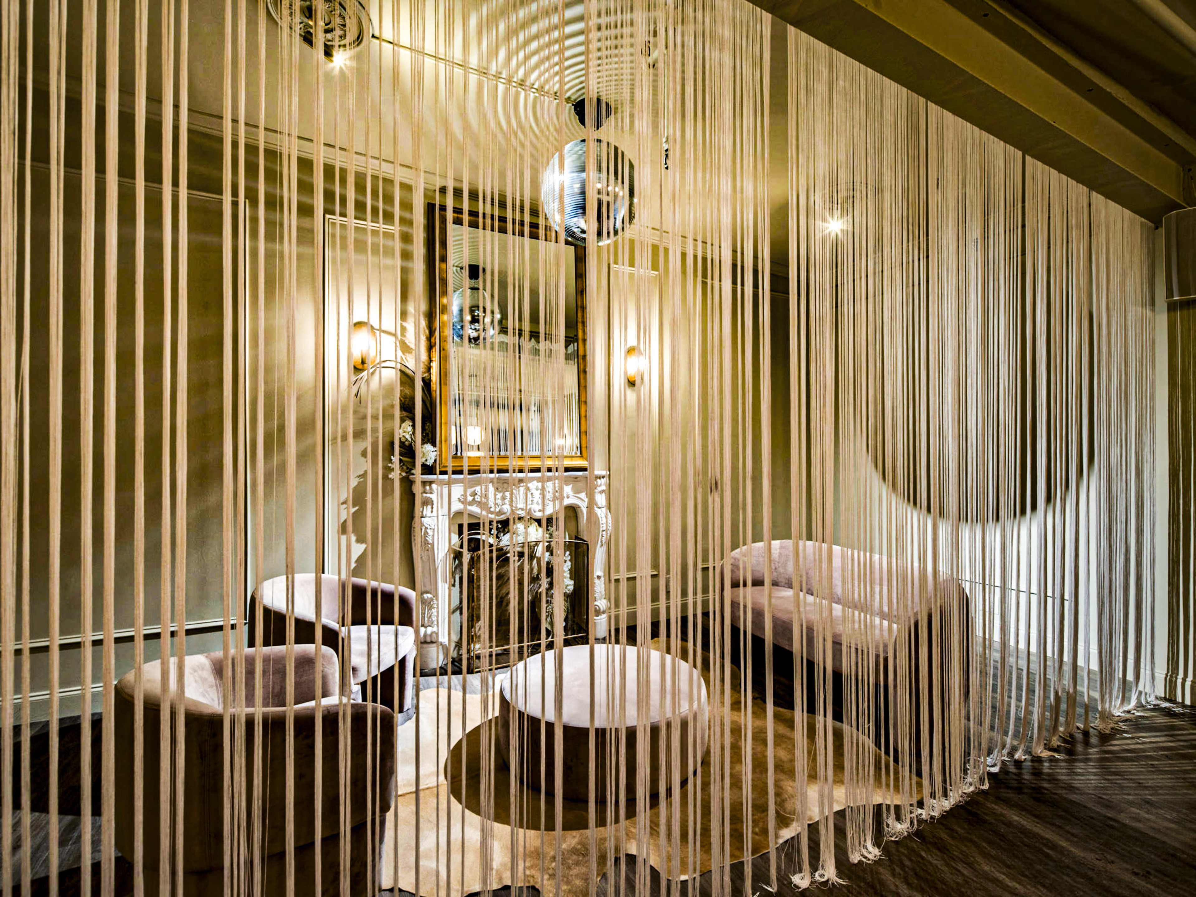 A lounge area features soft seating arranged around circular tables, divided by hanging sheer strands.