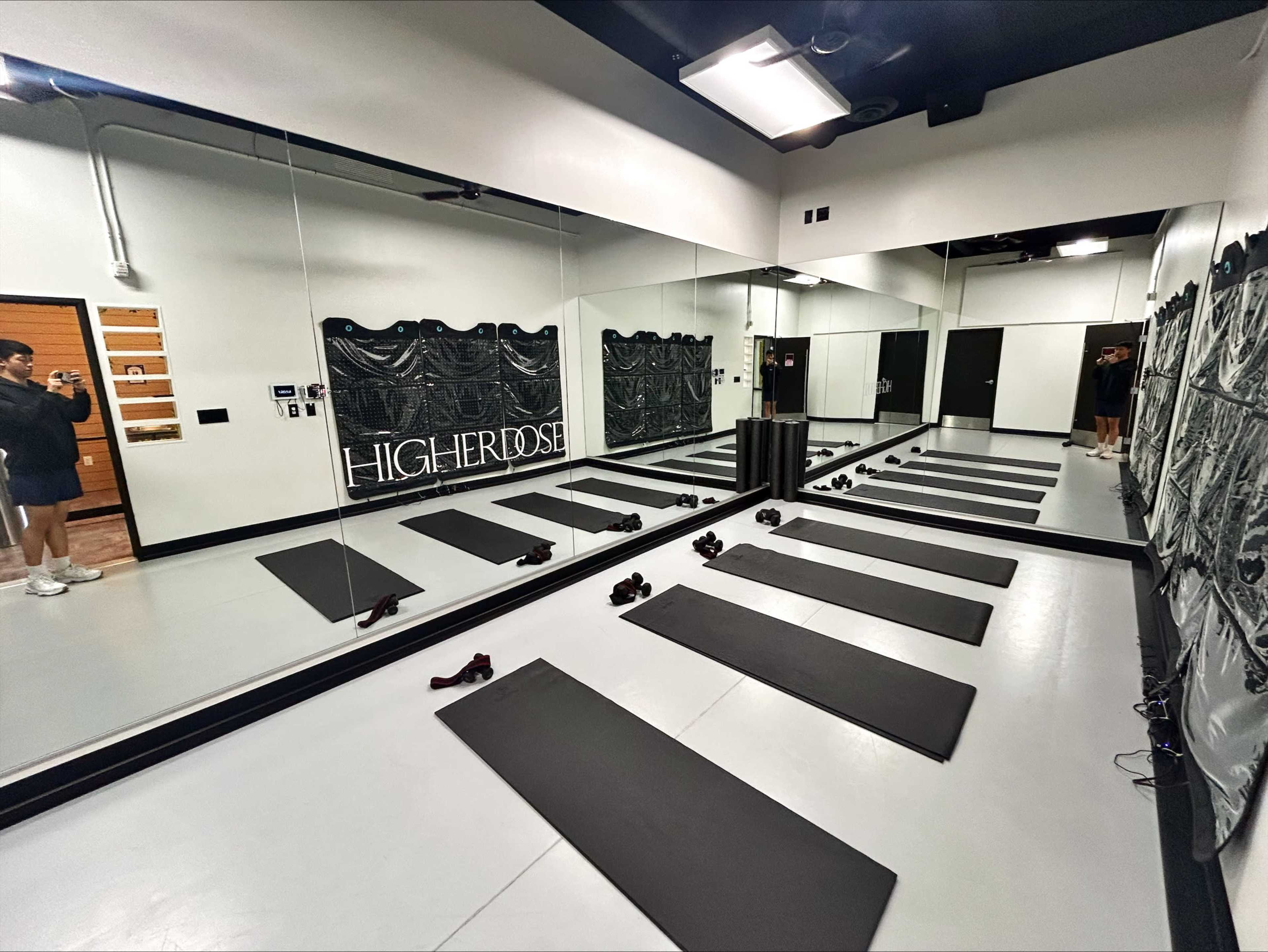 The image shows a yoga or fitness studio with mirrored walls and several exercise mats arranged on the floor.