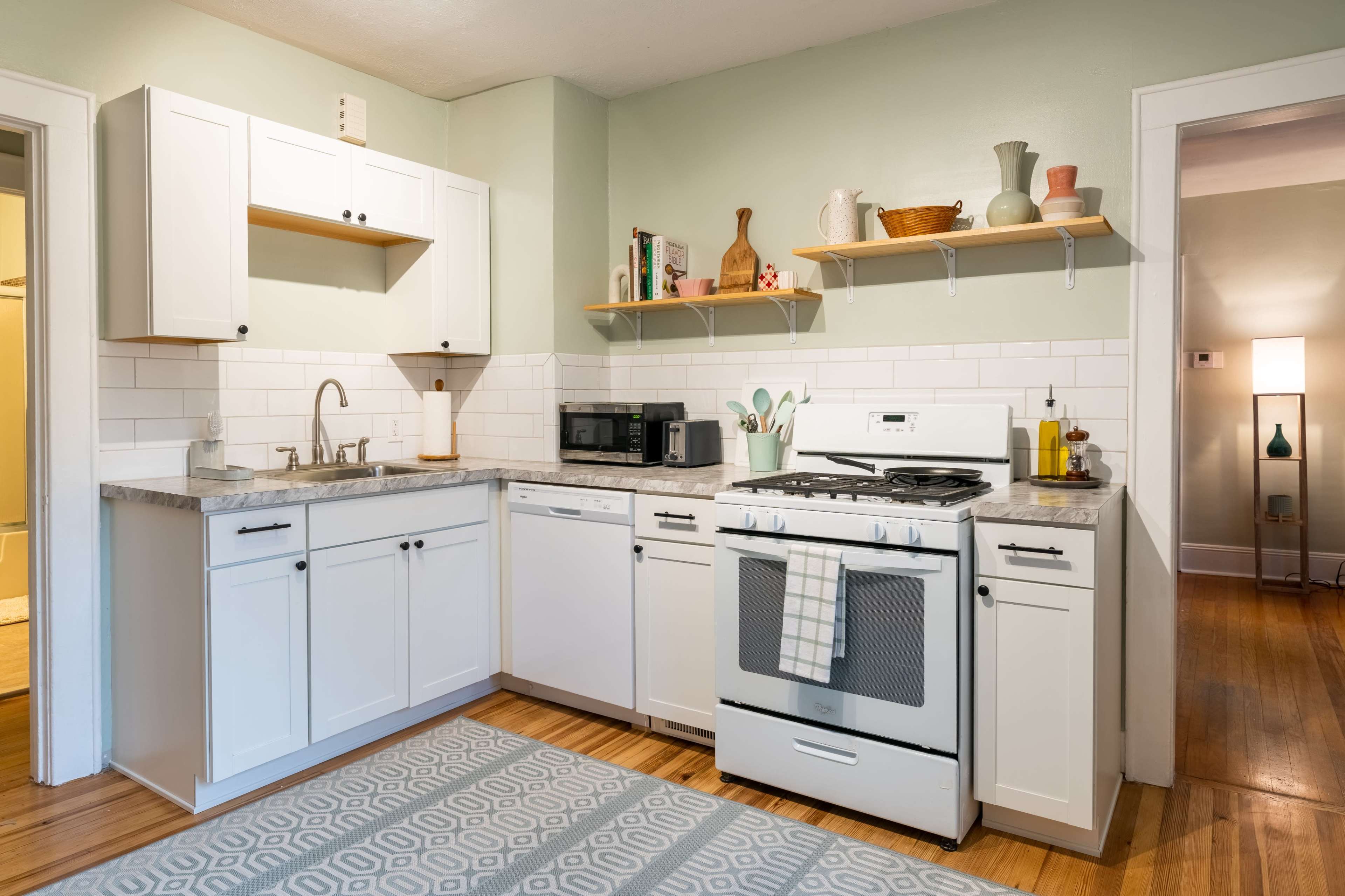 A modern kitchen with white cabinetry, a granite countertop, a gas stove, and shelves displaying various kitchen items.