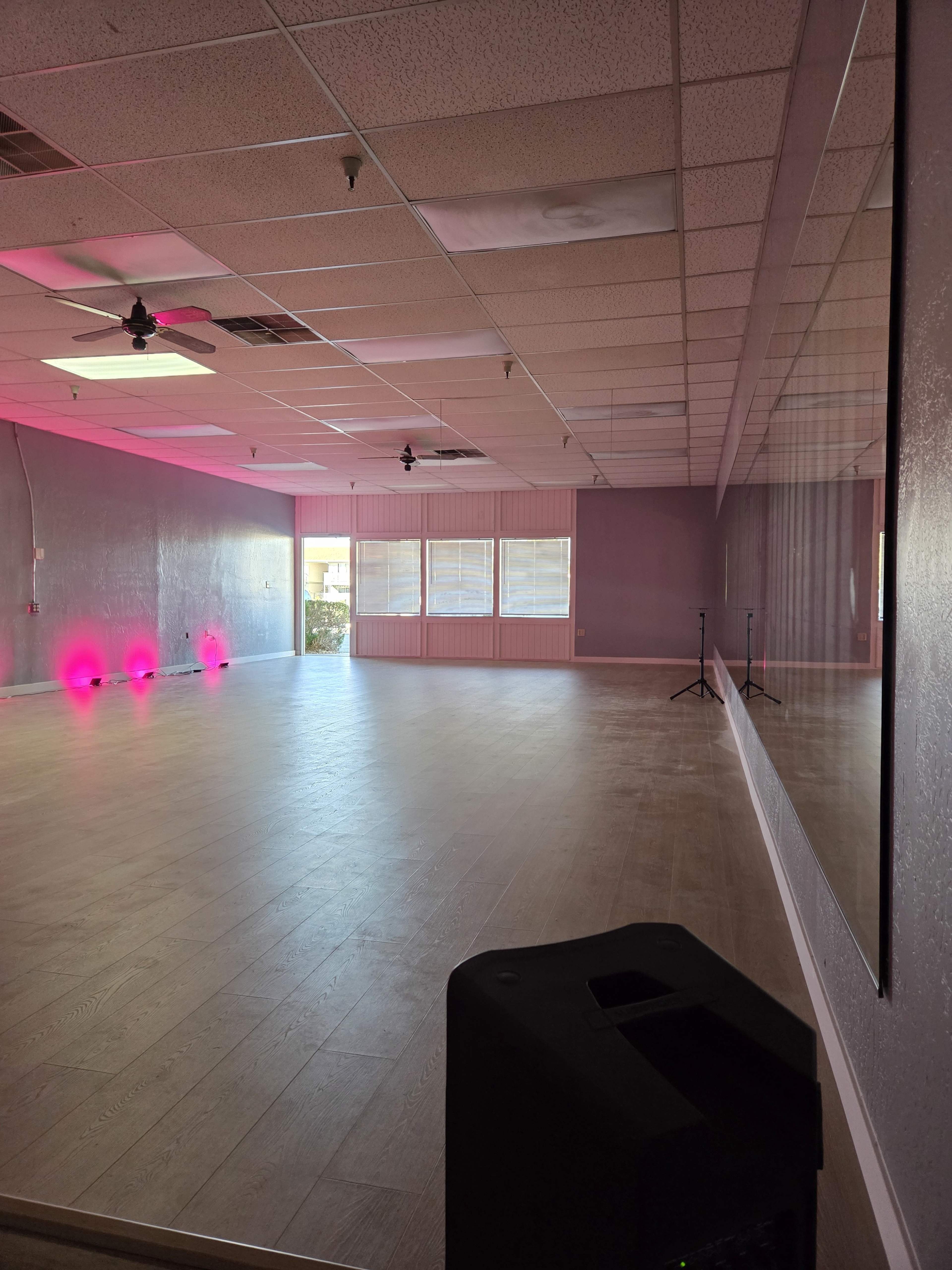 The image shows an empty dance studio with purple walls, a mirrored wall, and pink lighting accents.