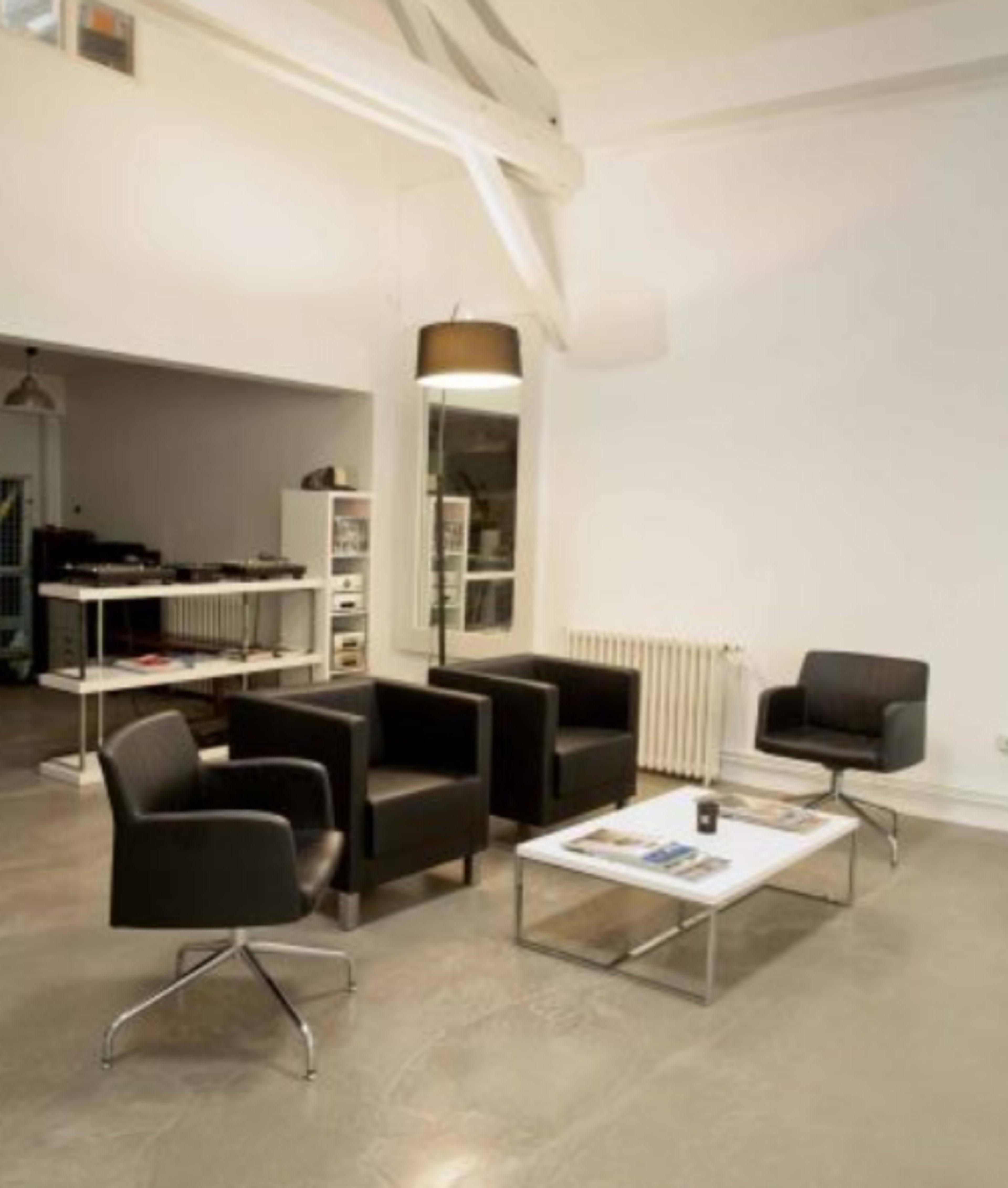 A modern interior space features four black armchairs arranged around a glass coffee table on a polished concrete floor.