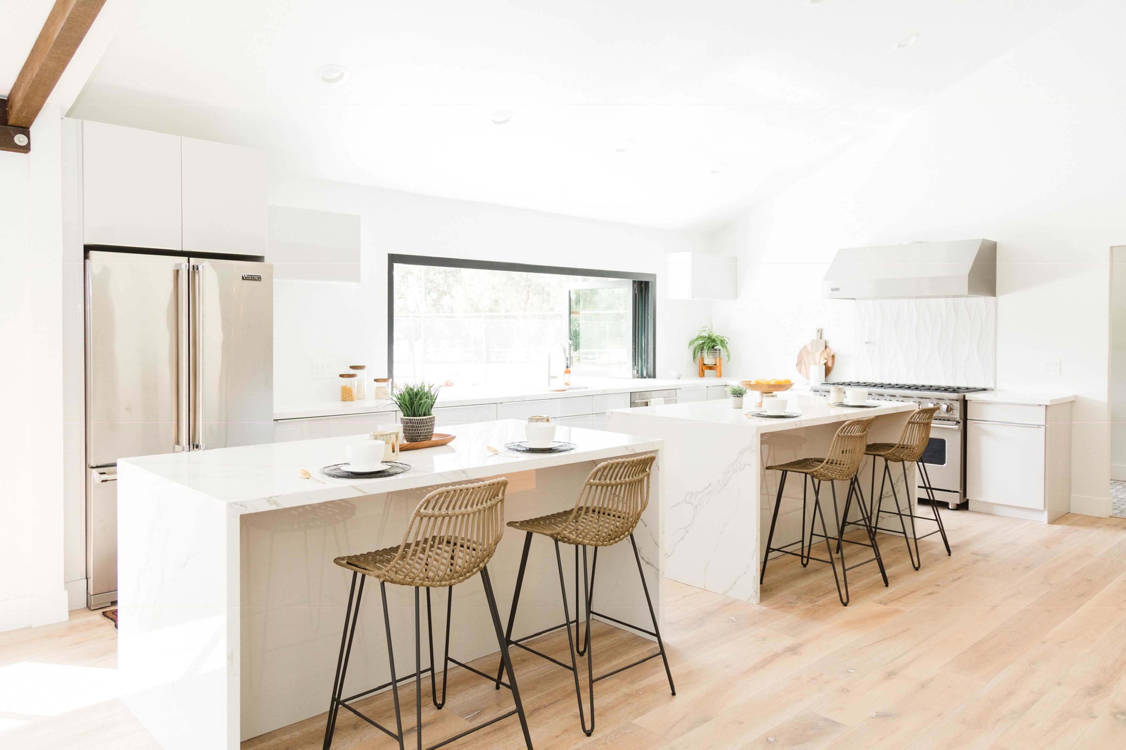 The image displays a modern kitchen with a large island, four bar stools, stainless steel appliances, and white cabinetry.