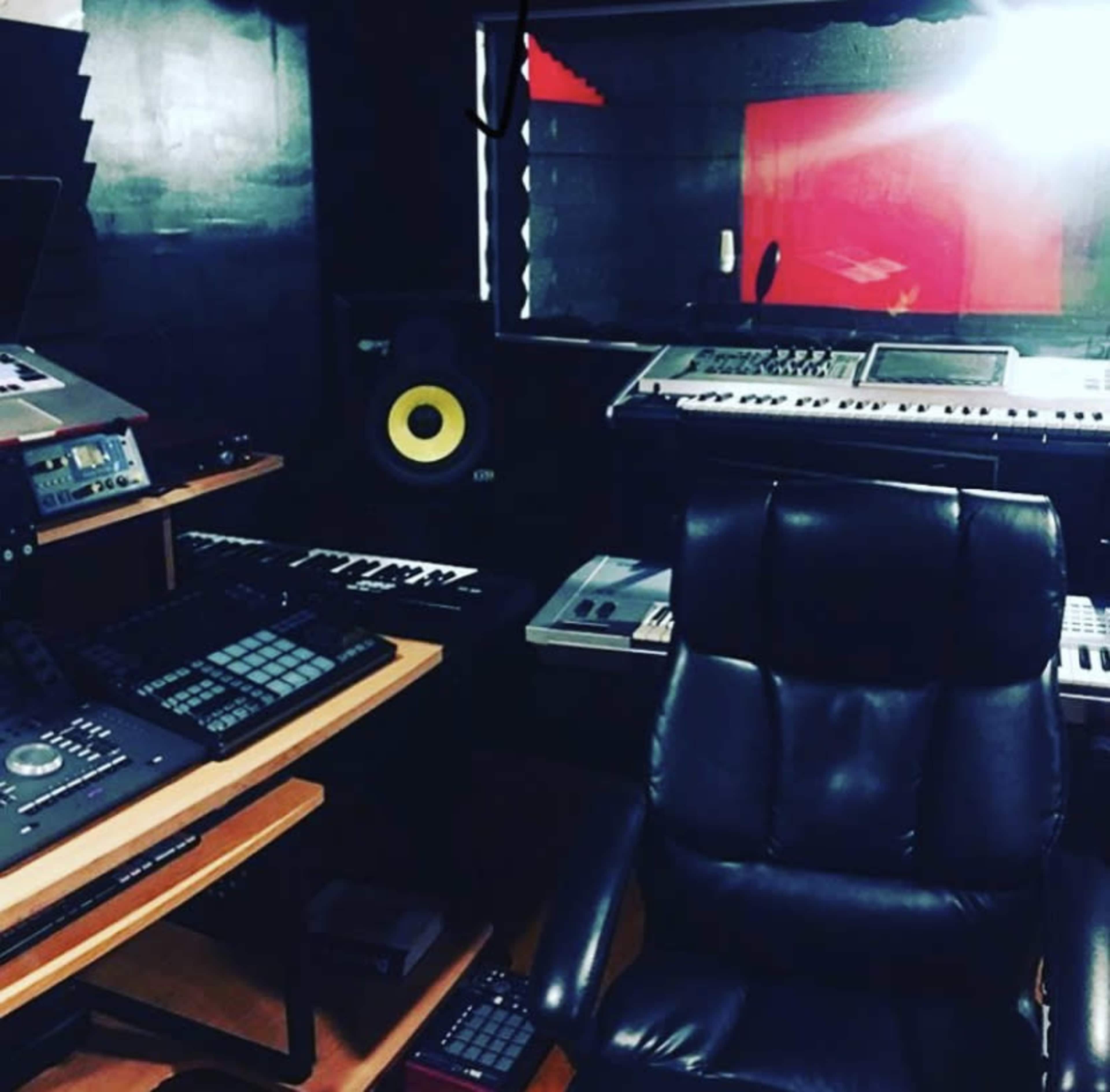 A music production studio with various keyboards, audio equipment, and a black ergonomic chair.