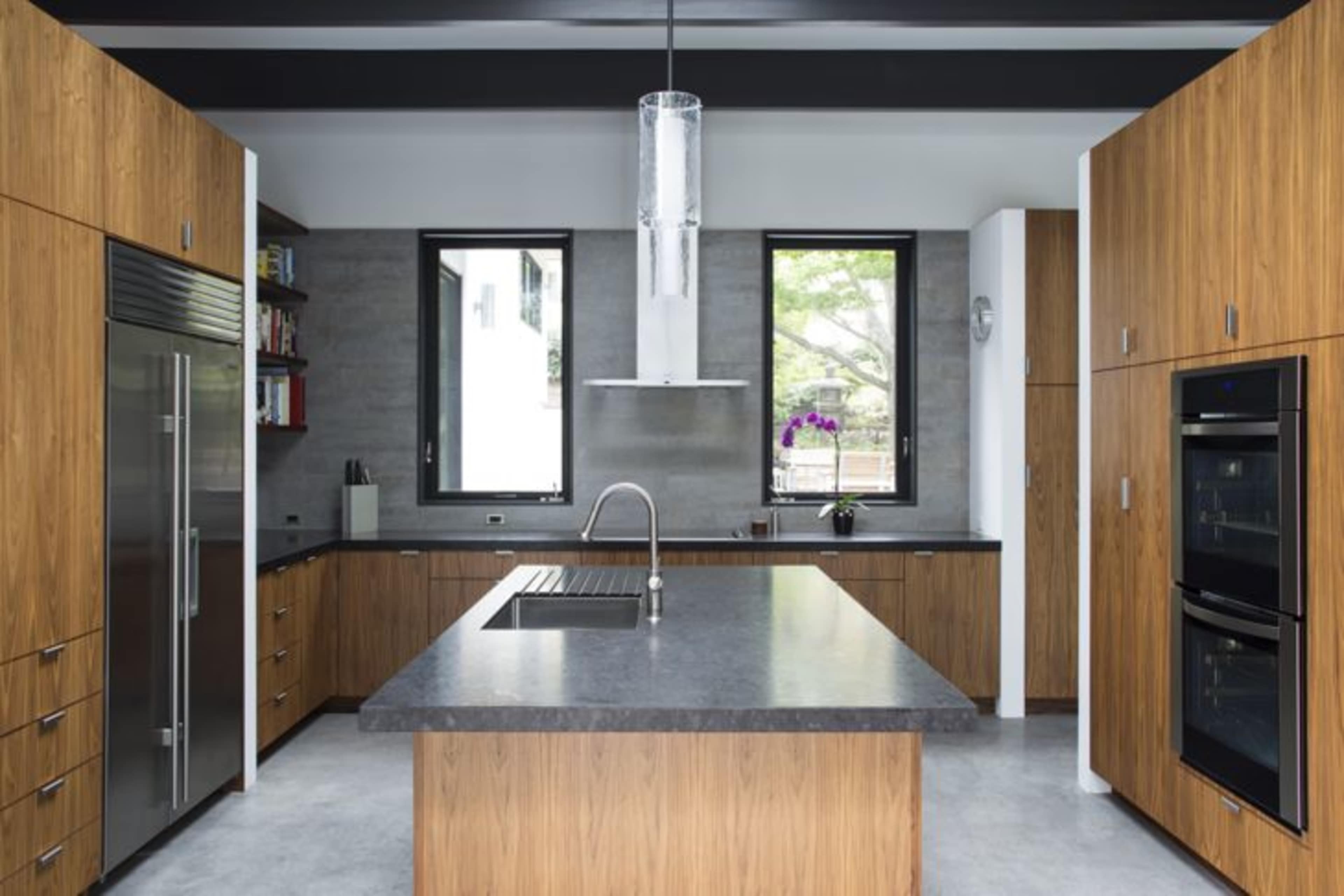 A modern kitchen with wooden cabinetry, a large central island, and stainless steel appliances, illuminated by a pendant light.
