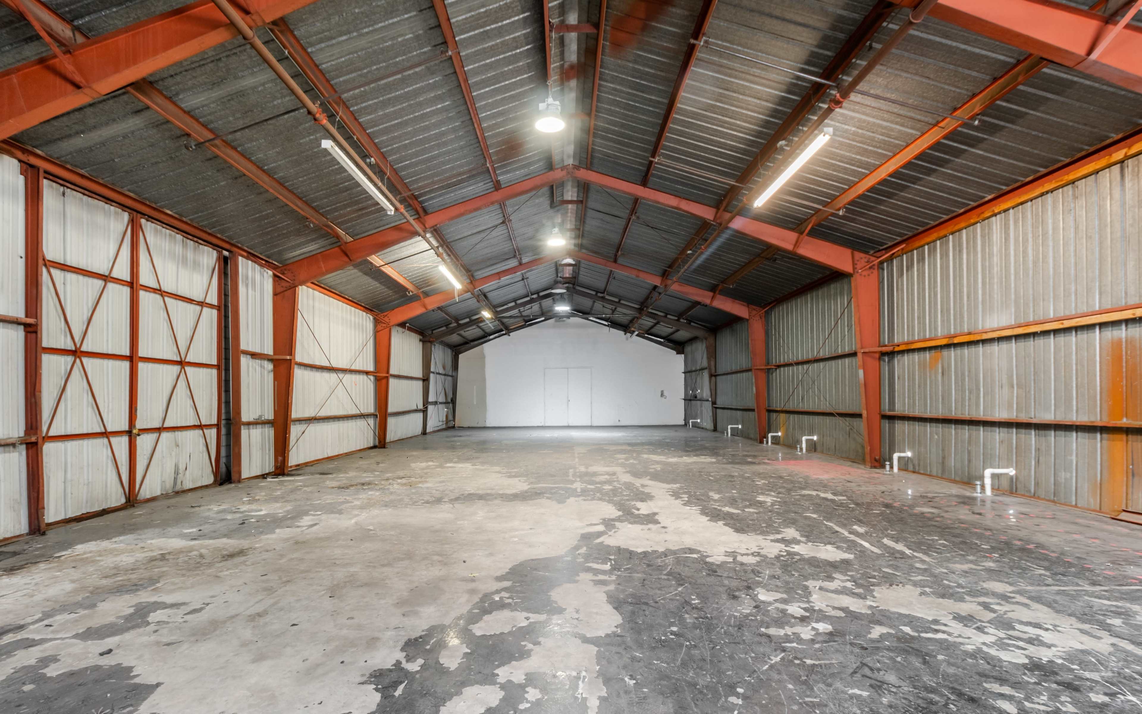 The interior of a large, empty warehouse with a high ceiling, metal beams, and concrete flooring.