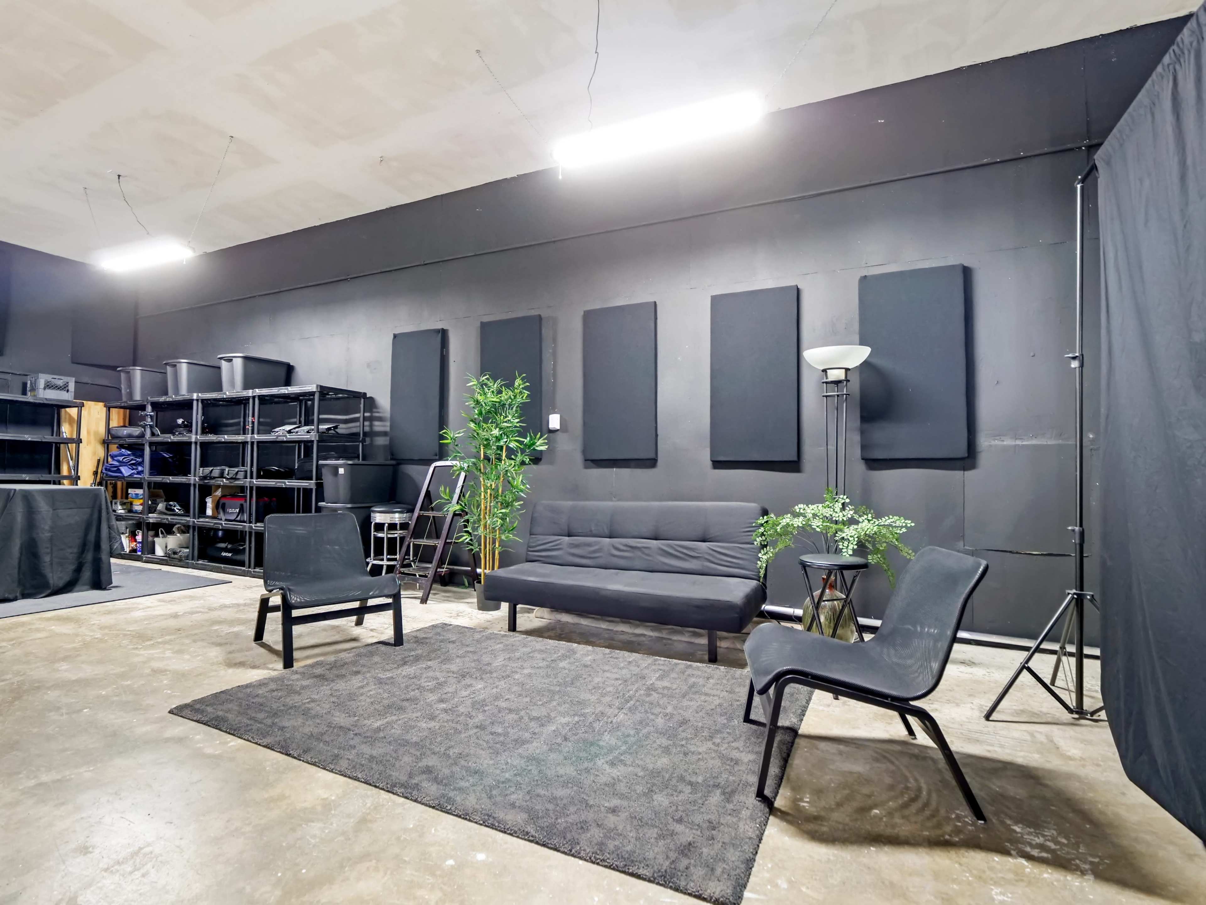 A minimalist room with black walls, a gray rug, a black couch, two chairs, and shelves filled with storage boxes.