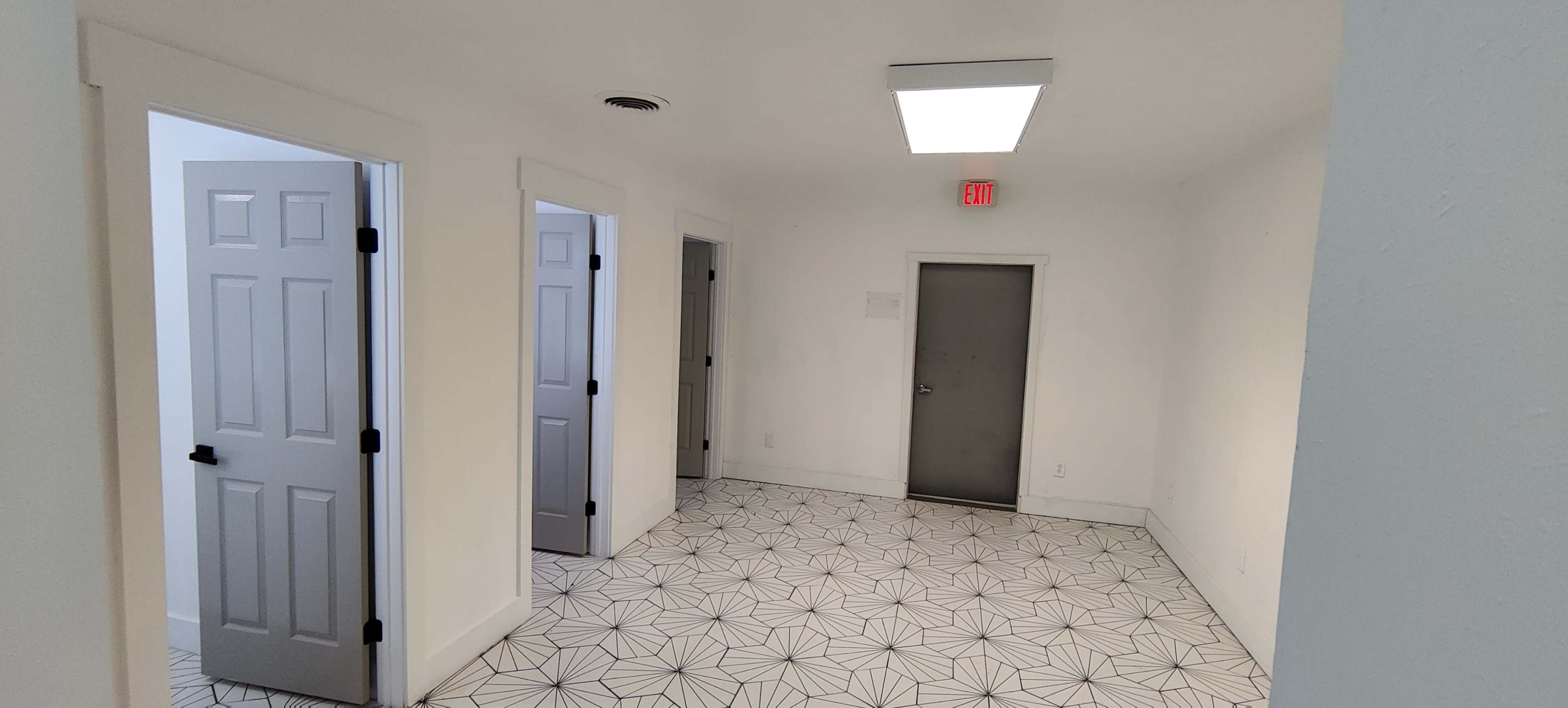 A bright, empty room with a geometric tile floor and three doorways leading to other spaces.