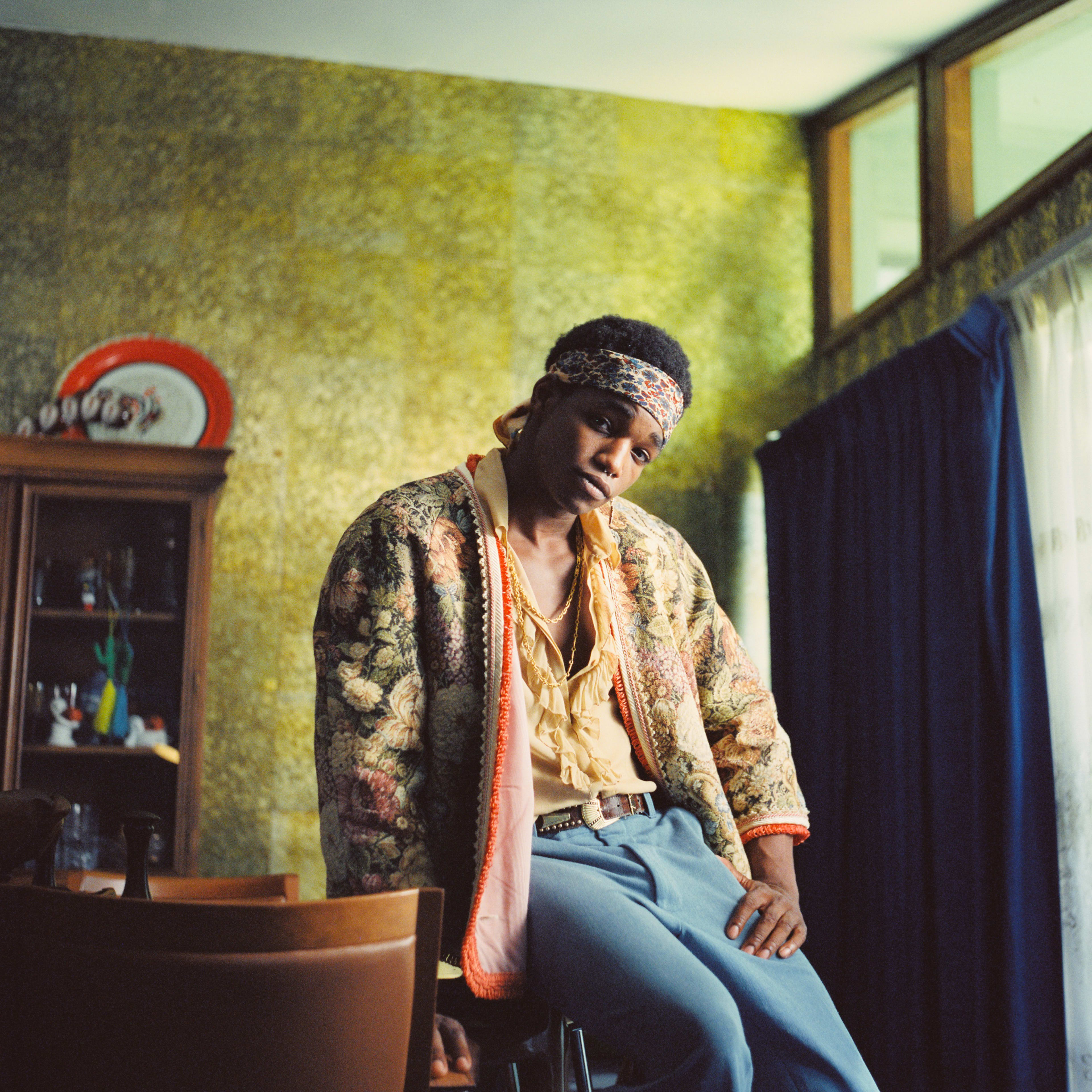 A man posing on a green chair for a retro 1960s fashion photo shoot.