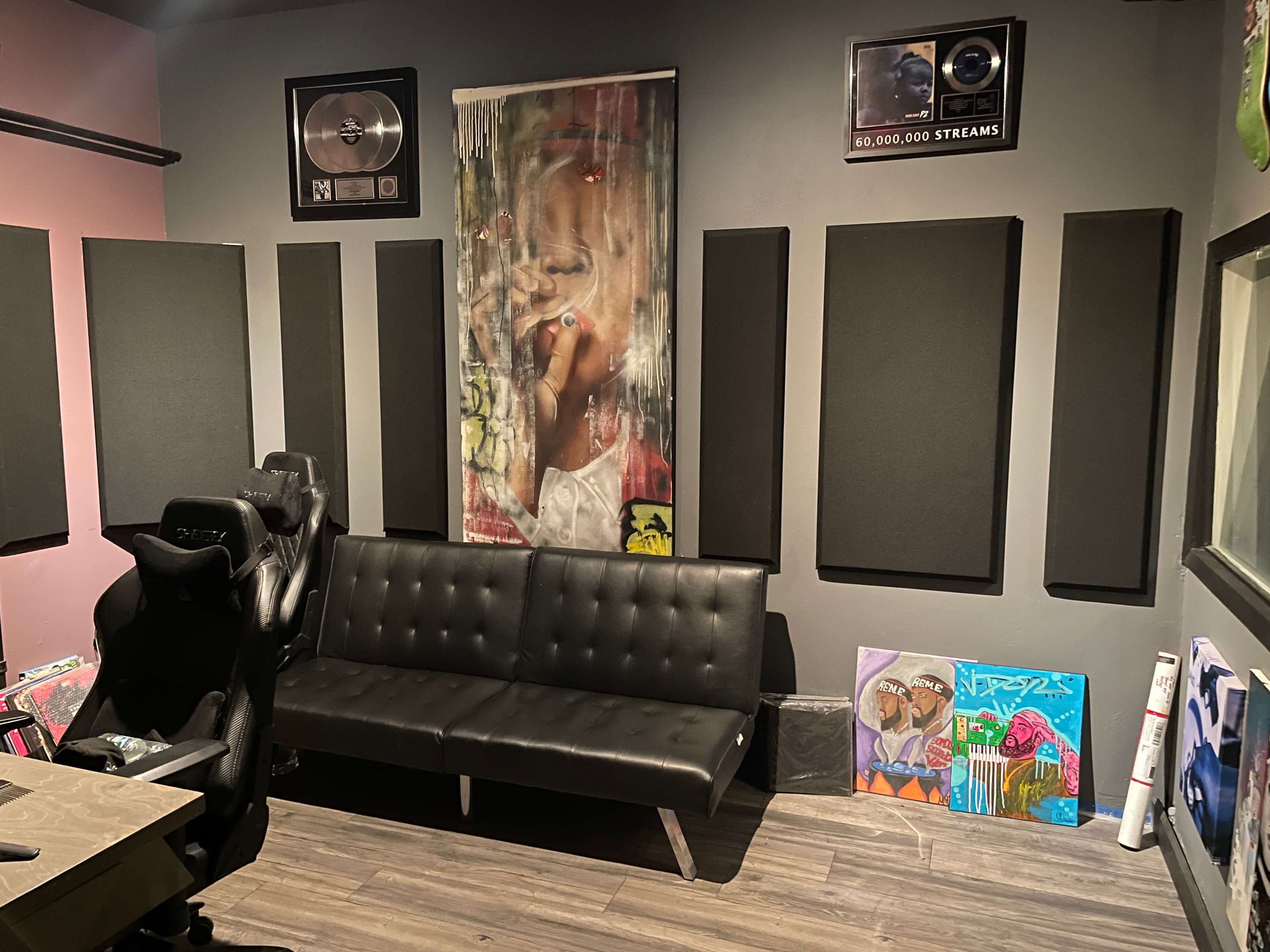 A recording studio with soundproofing panels on the walls, a black futon, and artwork displayed on the floor.
