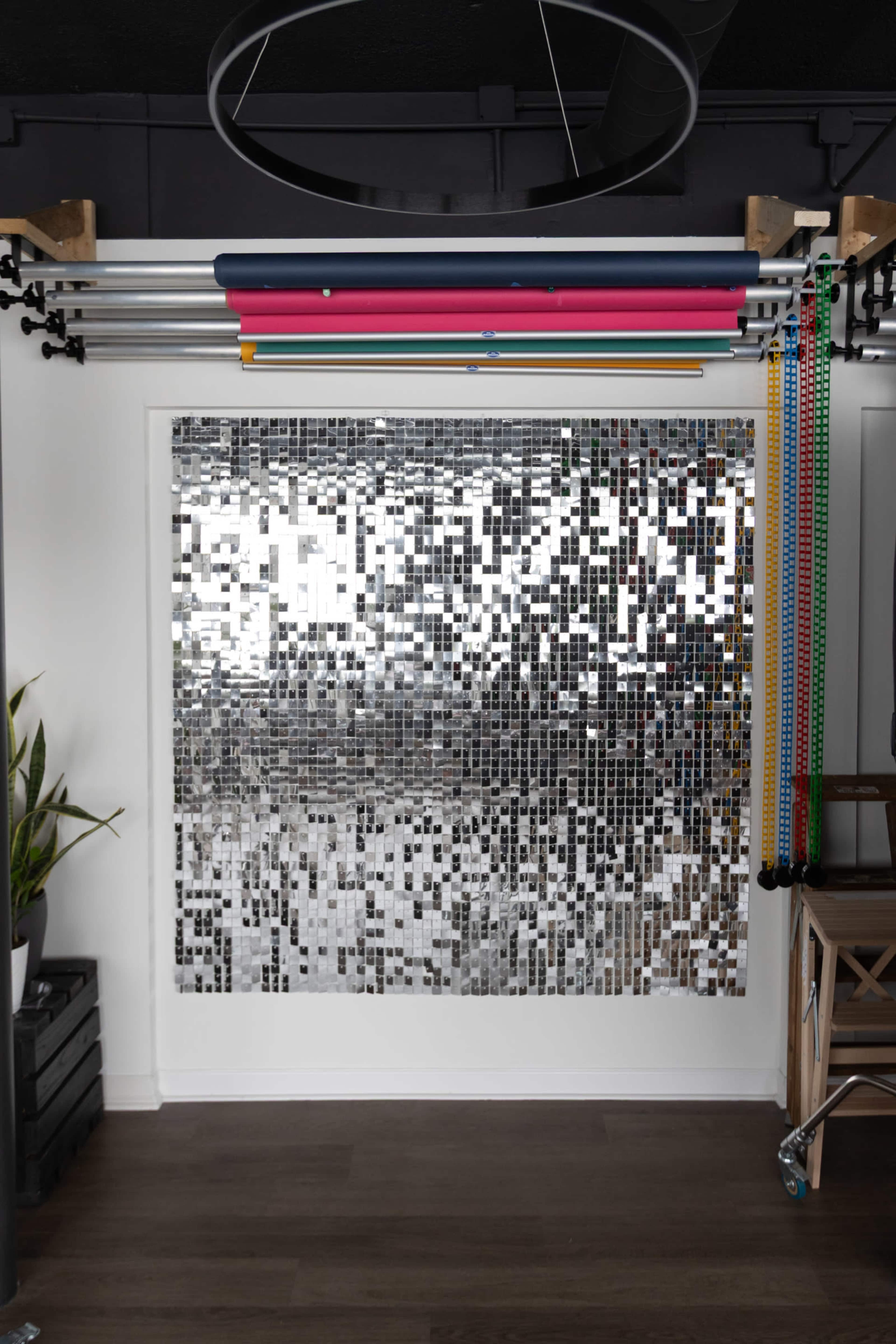 The image shows a wall covered in small, reflective tiles, with colorful exercise bands hanging from a rod above and a potted plant to the left.