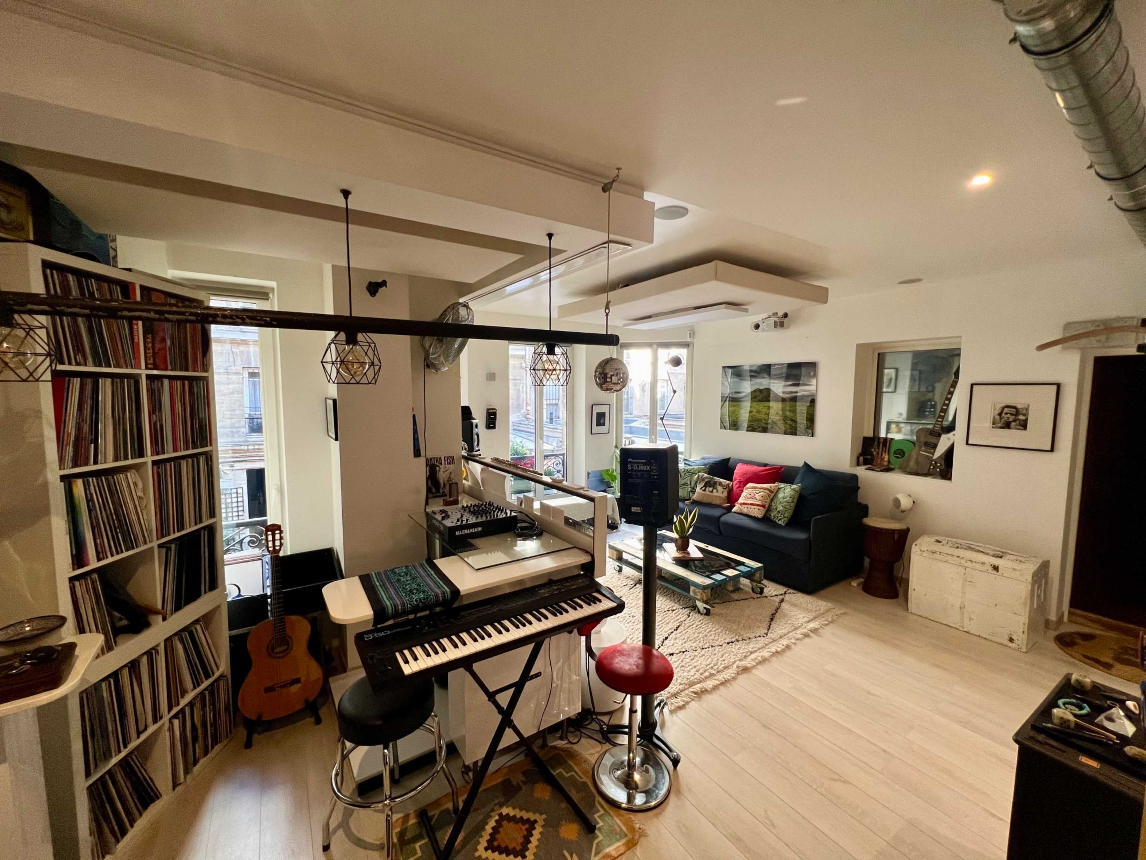 A cozy living space with a keyboard, record shelves, a guitar, and a seating area featuring a sofa and decorative items.