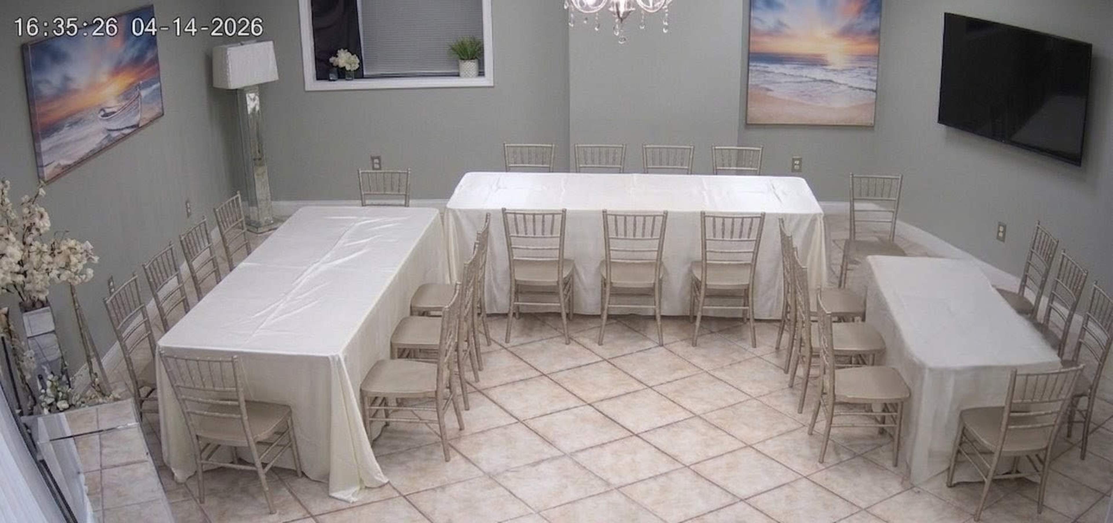 The image shows a banquet room arranged with multiple tables and chairs, featuring light-colored tablecloths and artwork depicting seascapes on the walls.