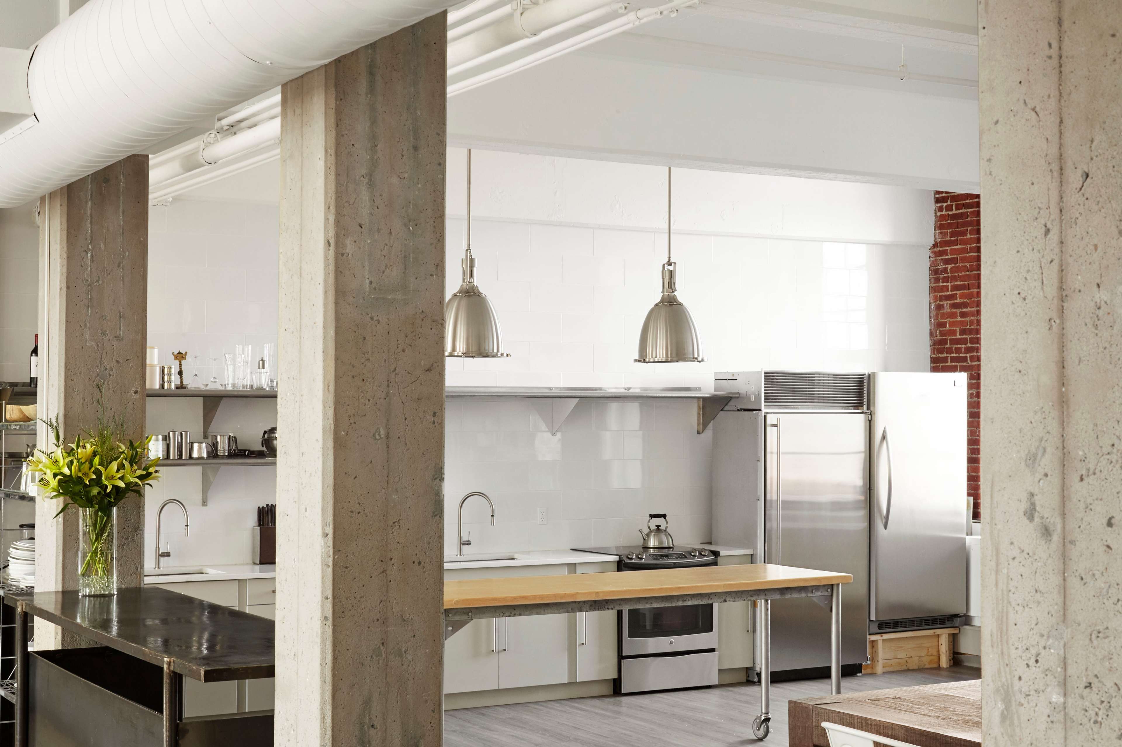 A modern kitchen with stainless steel appliances, a central wooden island, and concrete structural columns.