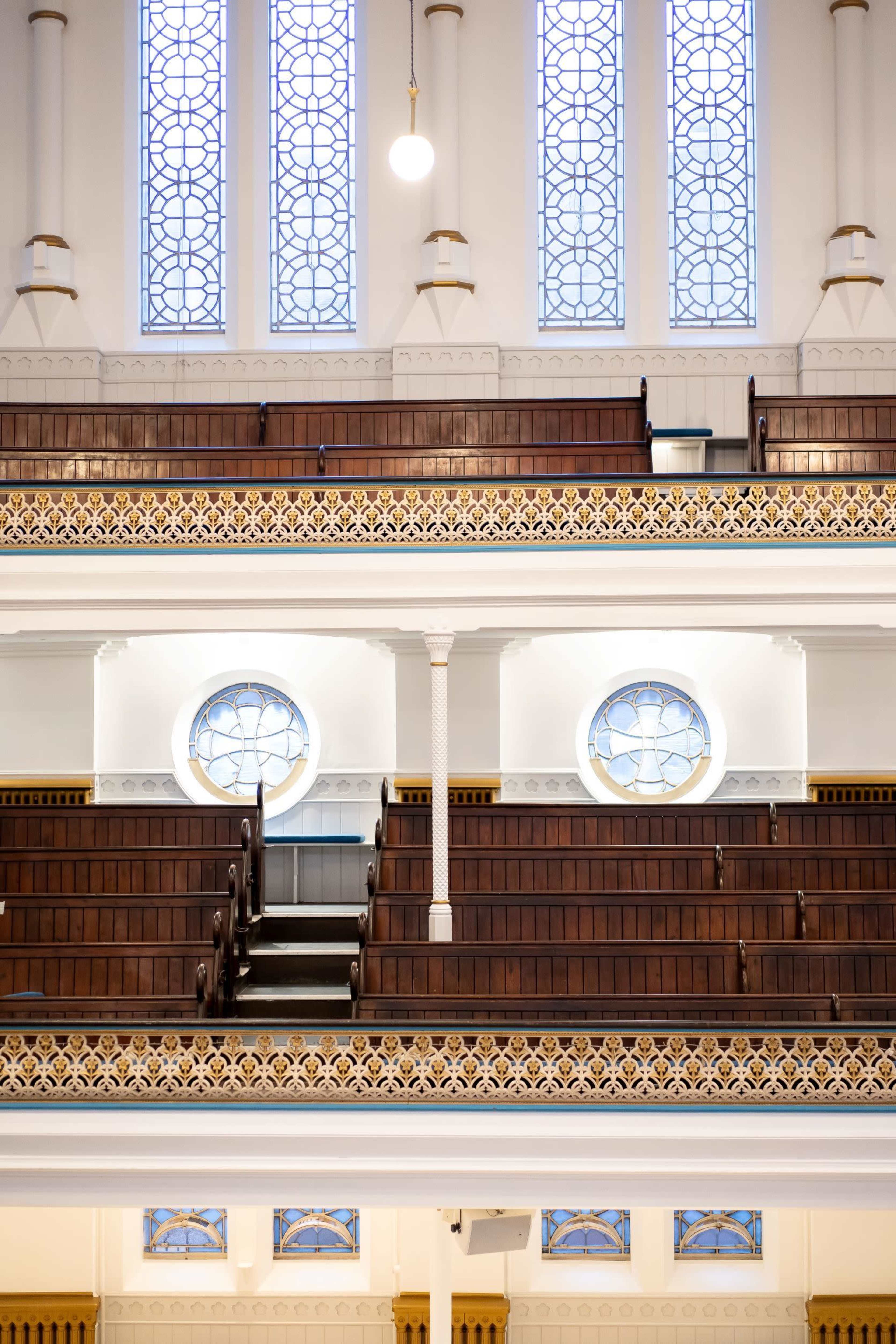 The interior of a church with wooden pews arranged in rows beneath stained glass windows.