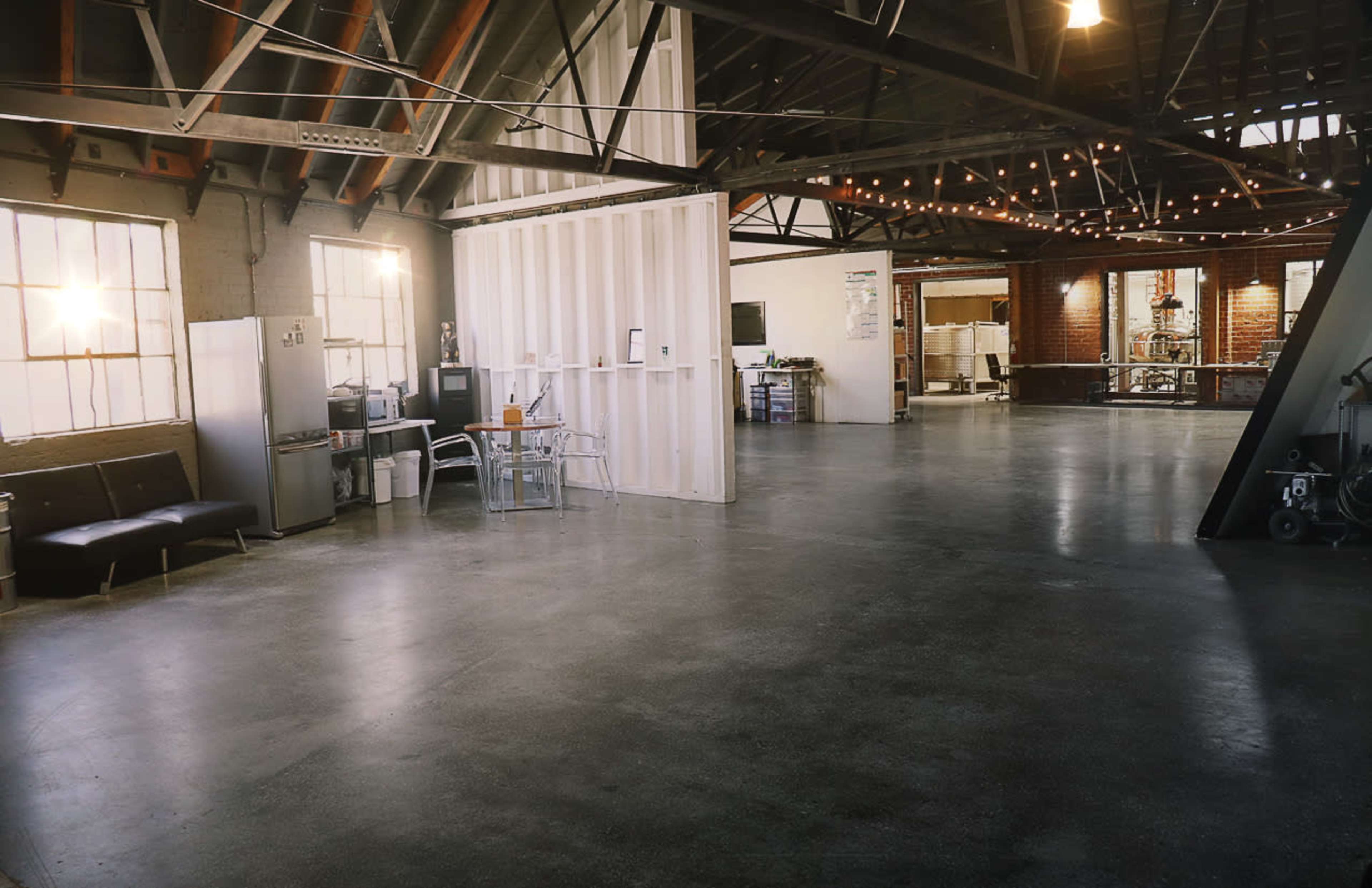 A spacious industrial loft with high ceilings, large windows, and polished concrete floors, featuring a few scattered pieces of furniture and workspaces.