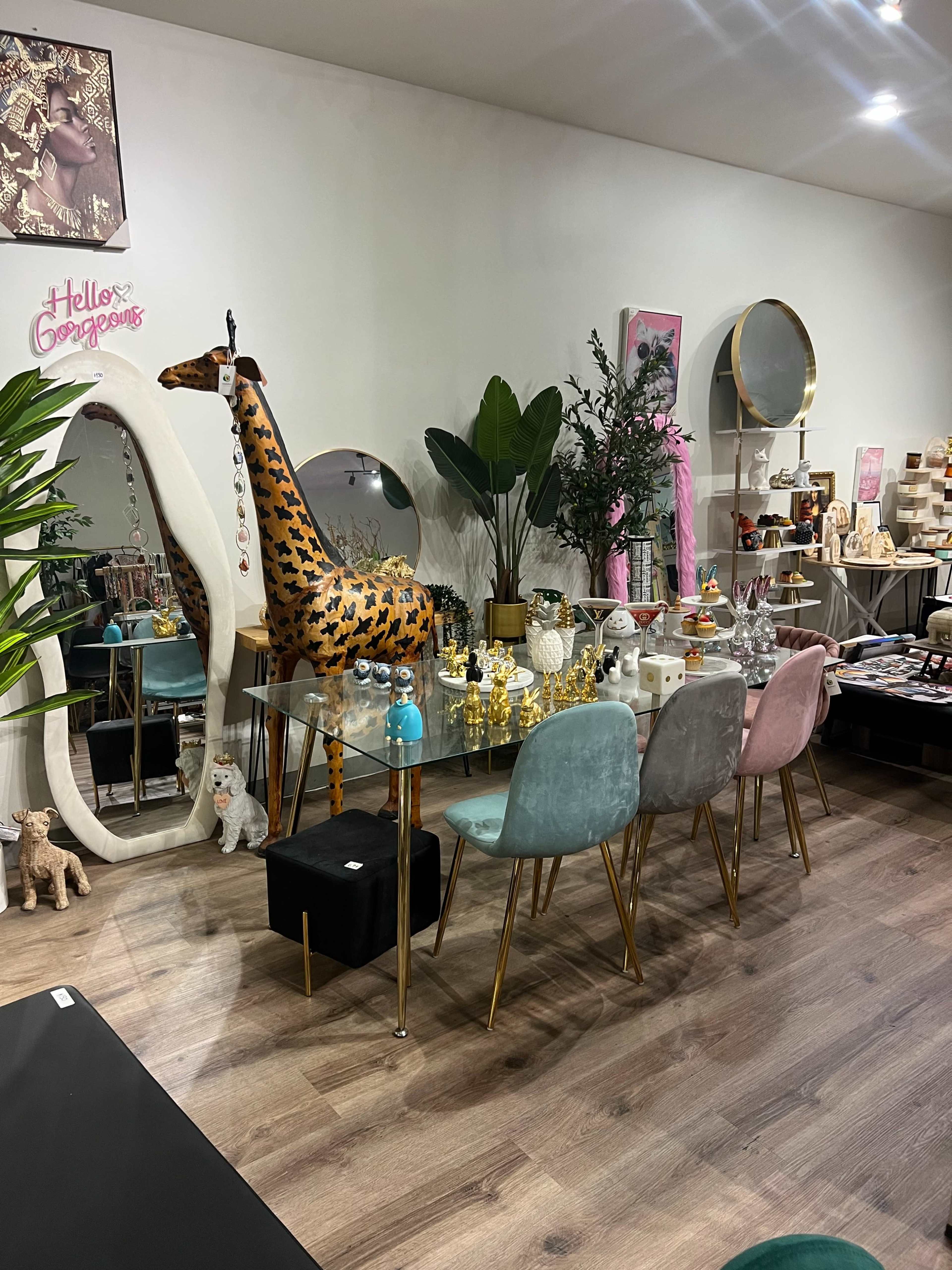 A modern interior space features a glass dining table surrounded by pastel-colored chairs, with decorative items and a large artistic giraffe sculpture nearby.