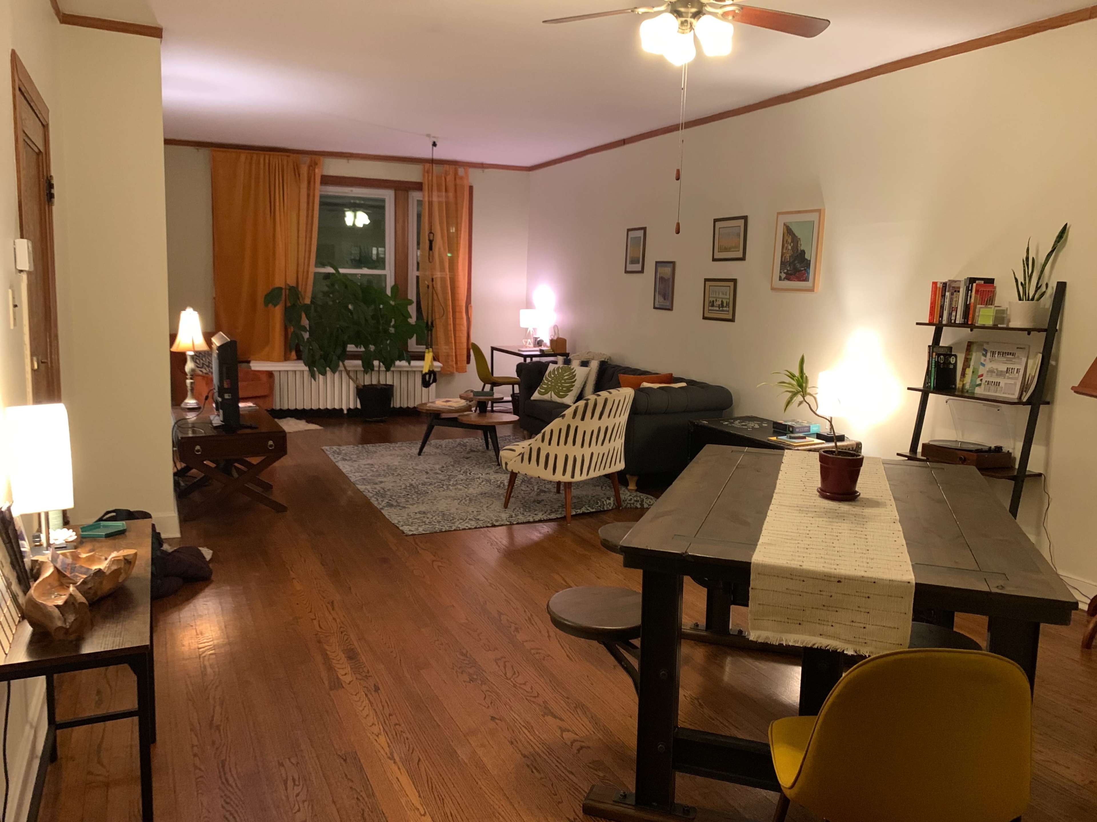 A well-furnished living room with wooden floors, a dining table, a sofa, and various lamps illuminating the space.