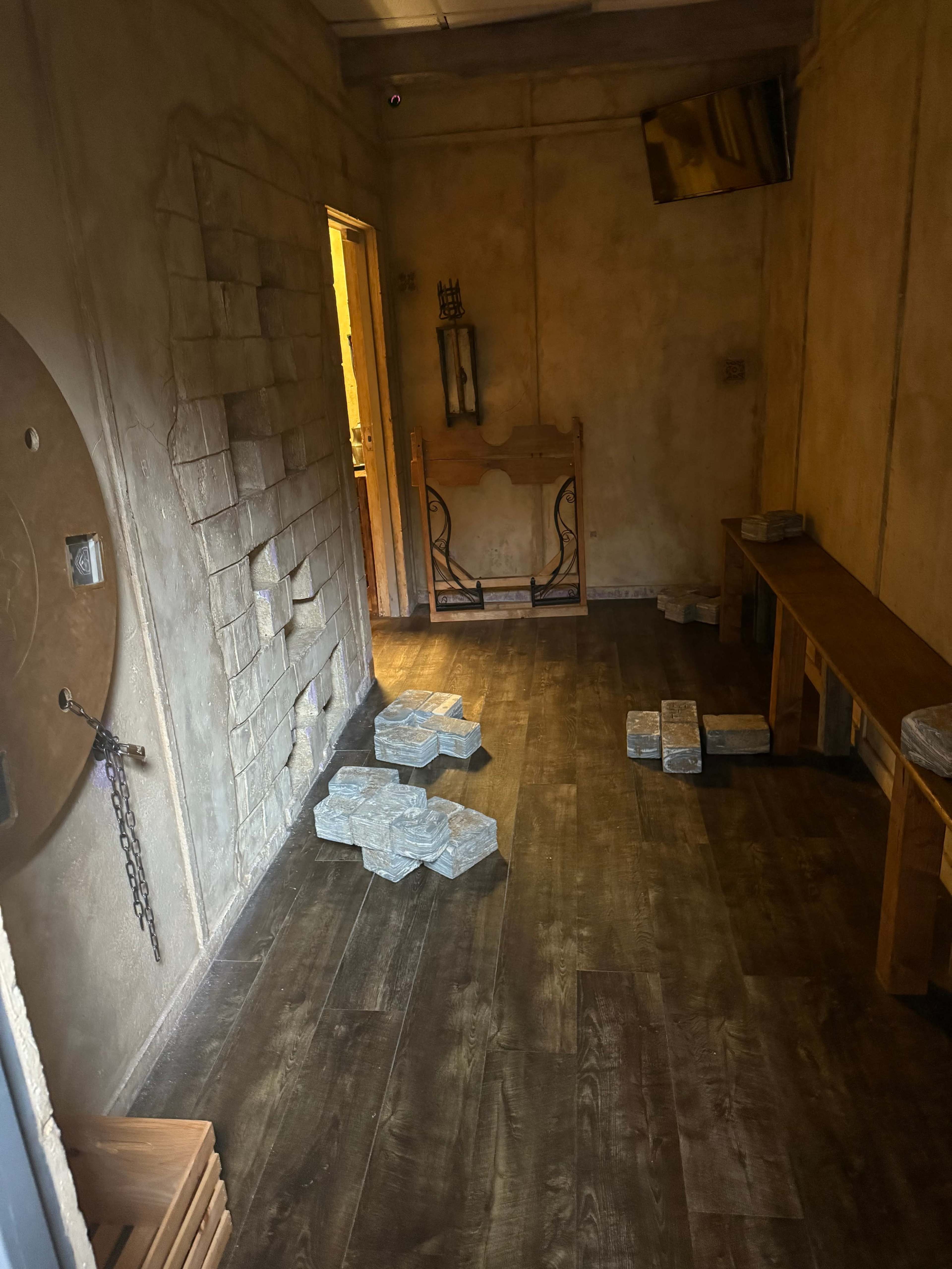 The image shows an empty room with textured walls, a wooden bench, scattered stone-like pieces on the floor, and a doorway leading to another area.