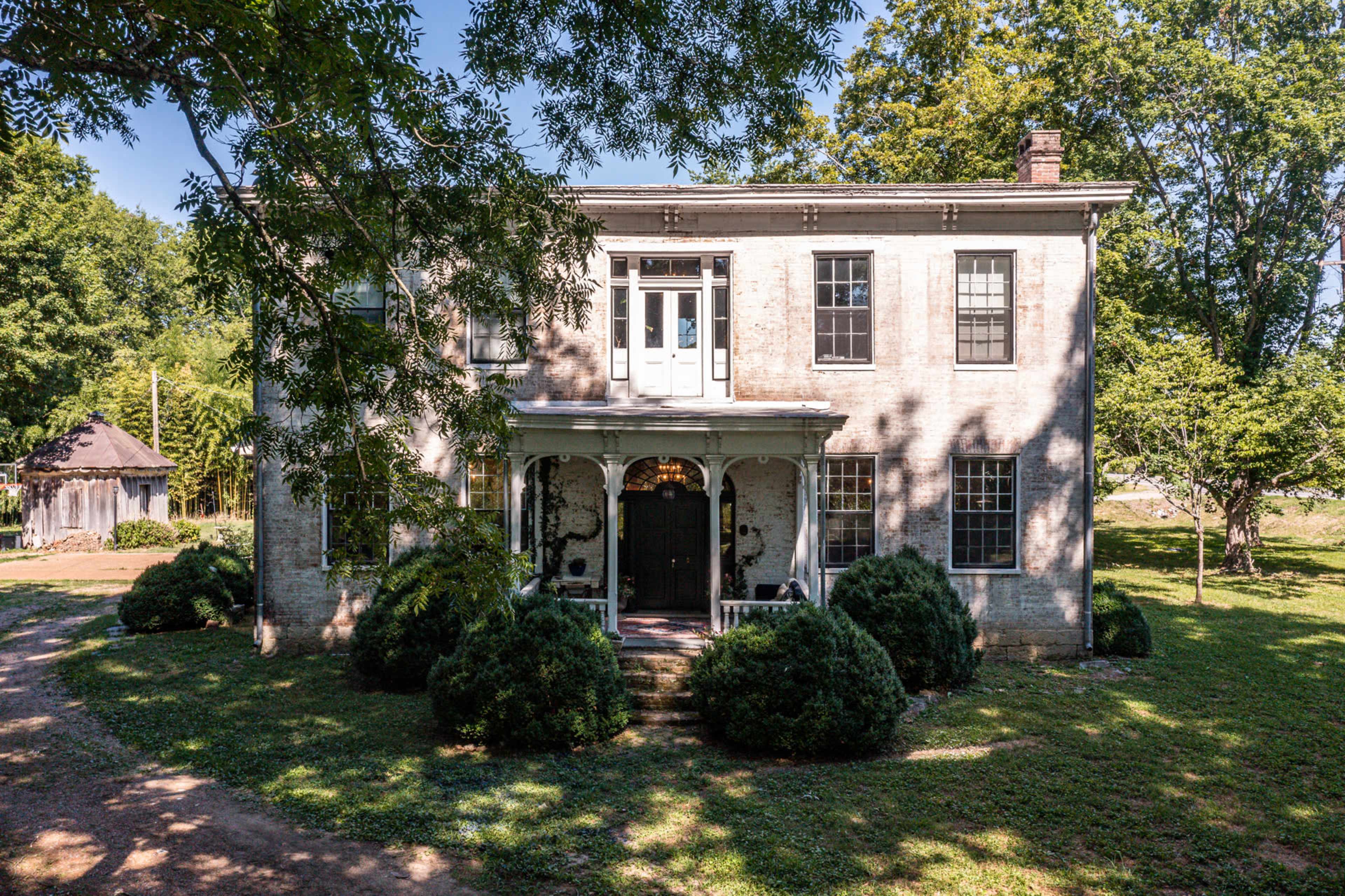 A two-story, rectangular brick house with a central entrance and surrounded by manicured shrubs on a grassy lawn.