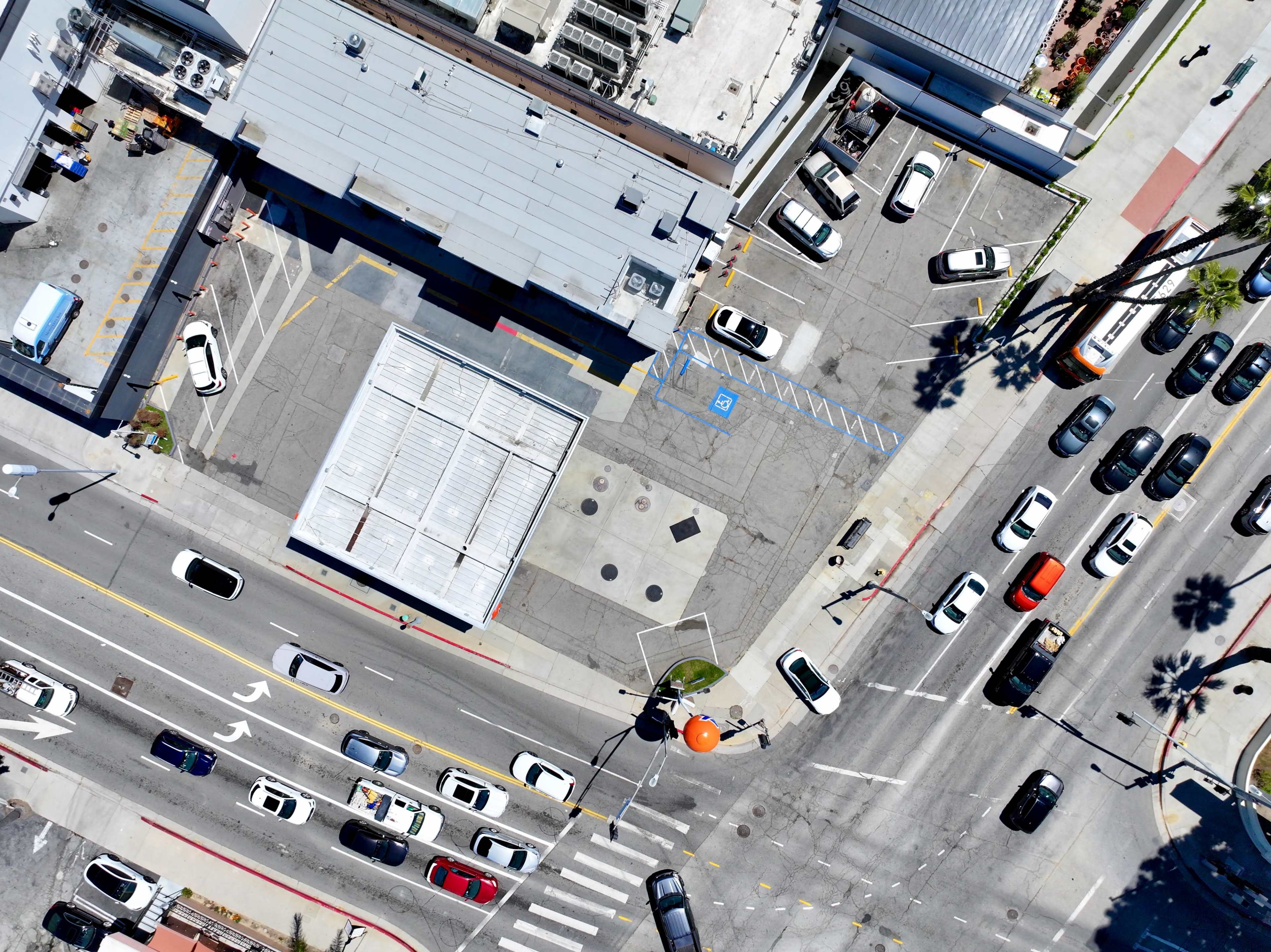 An aerial view captures a busy intersection with cars and a large orange balloon, surrounded by parking lots and buildings.