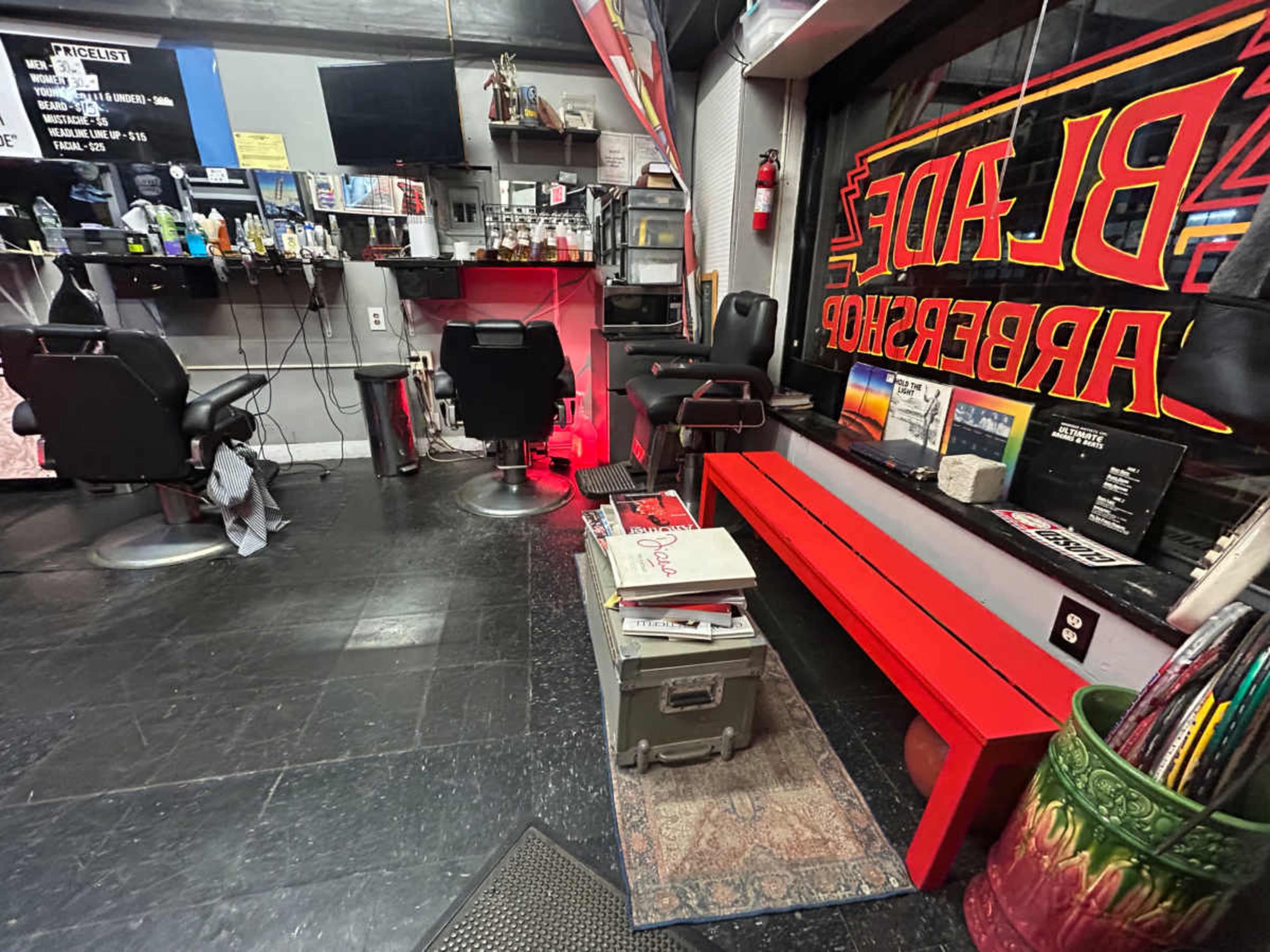 The image shows a barber shop interior with two styling chairs, a red bench, and various grooming tools displayed on a counter.