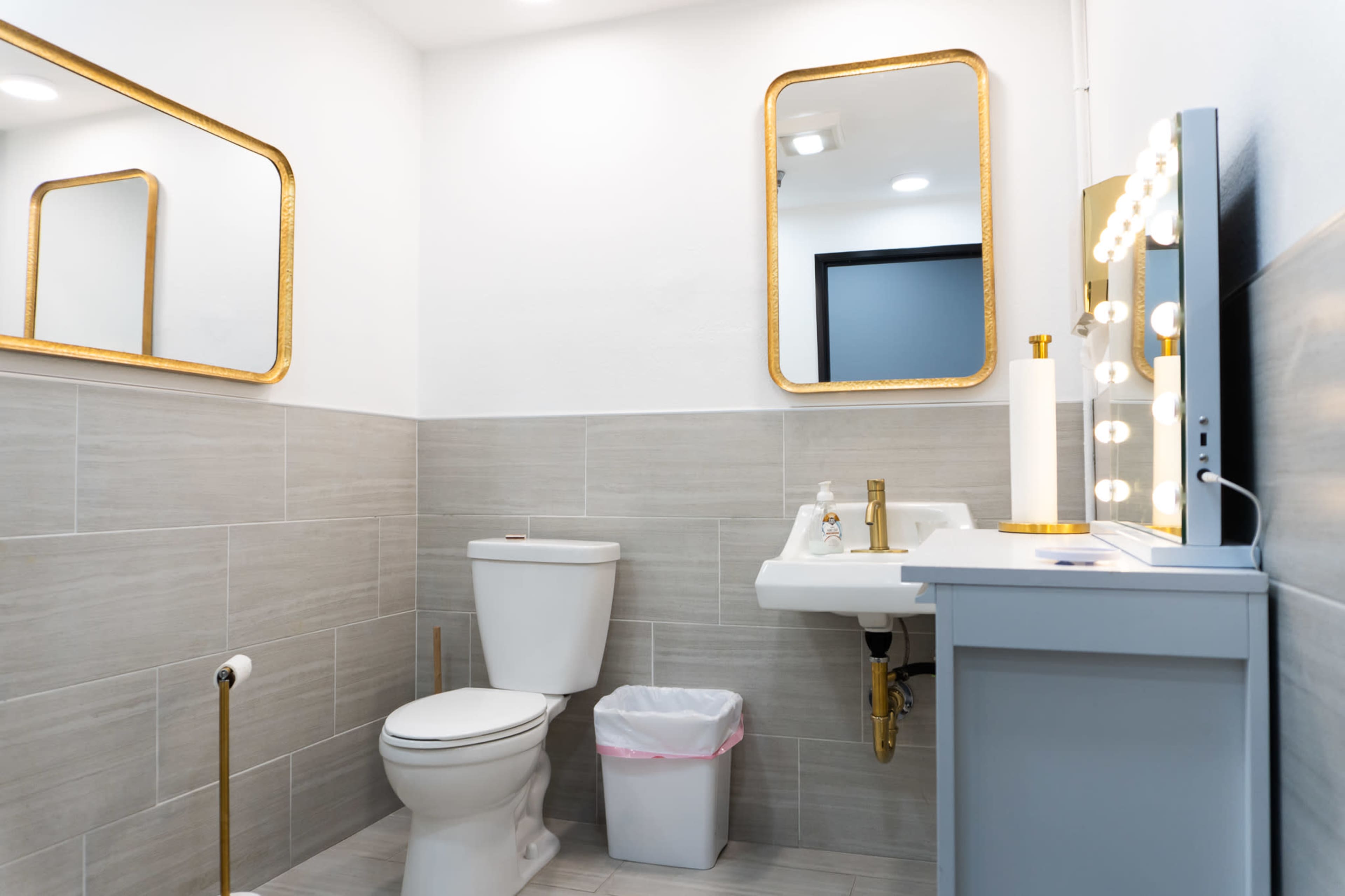 A modern bathroom features a toilet, a sink with a mirror, and decorative lighting, with light-colored tile on the walls and floor.