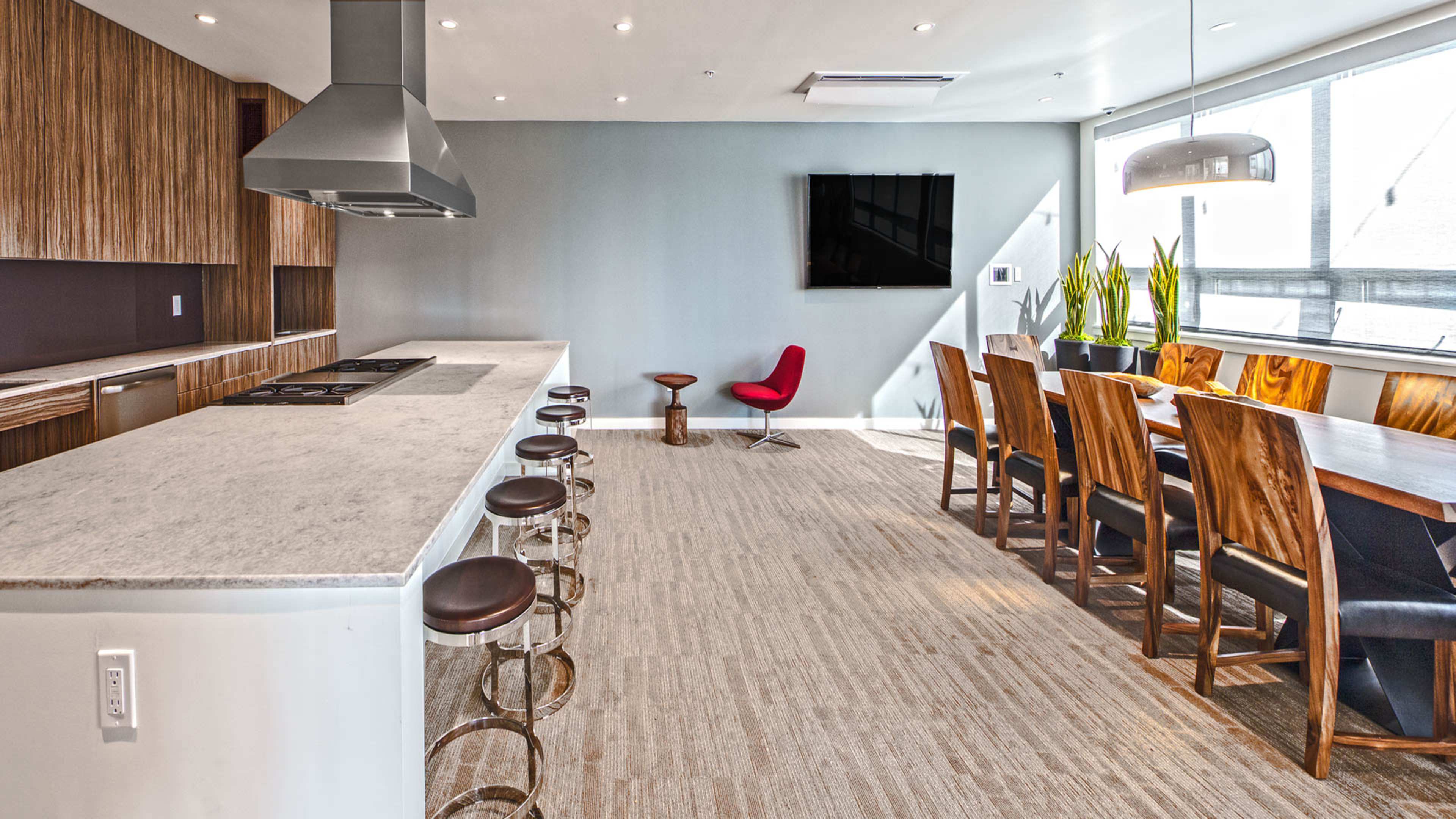 A modern kitchen and dining area features a large island with bar seating, wooden dining chairs around a long table, and a wall-mounted television.