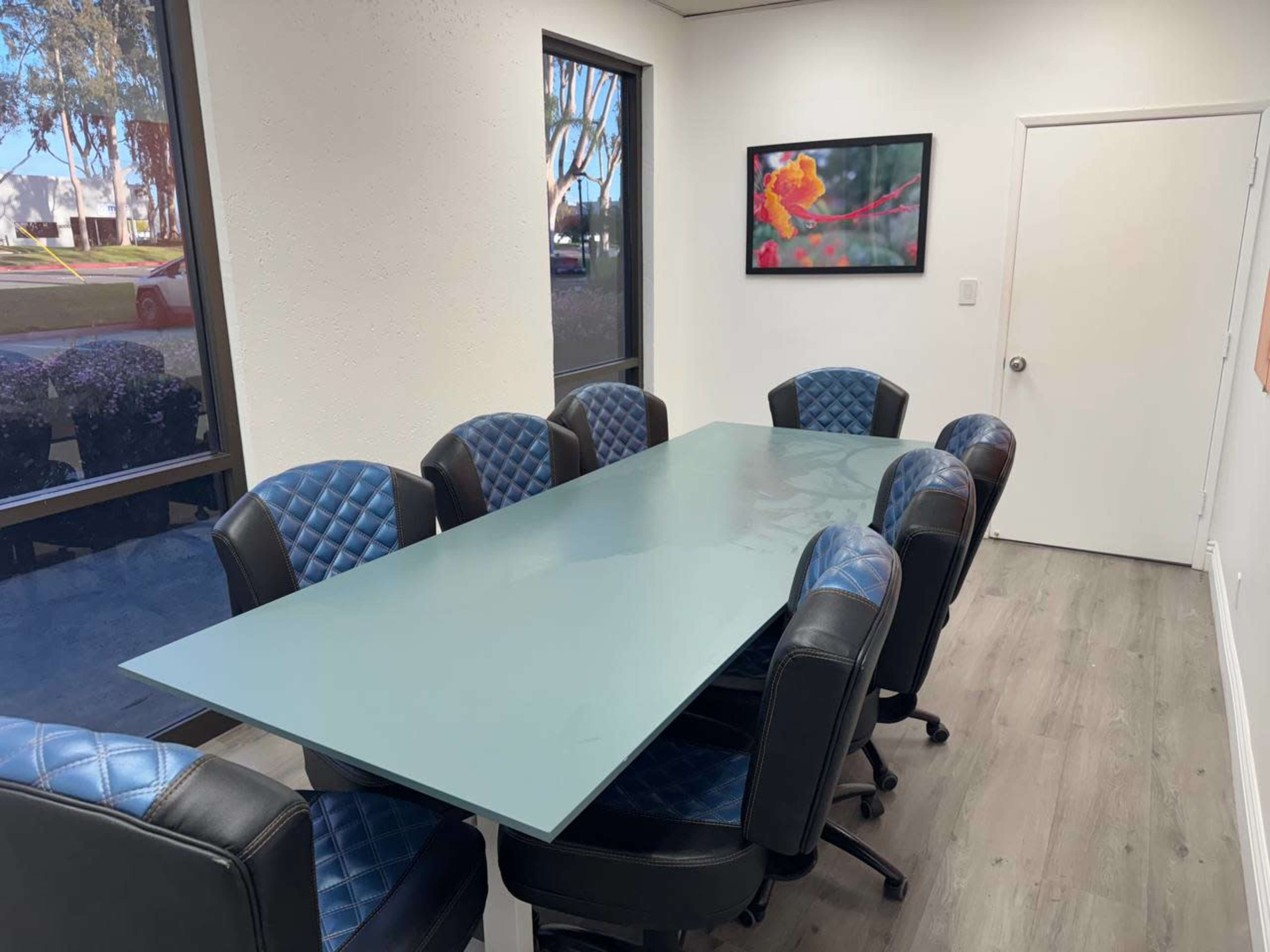 A long glass conference table is surrounded by eight leather chairs in a modern meeting room.