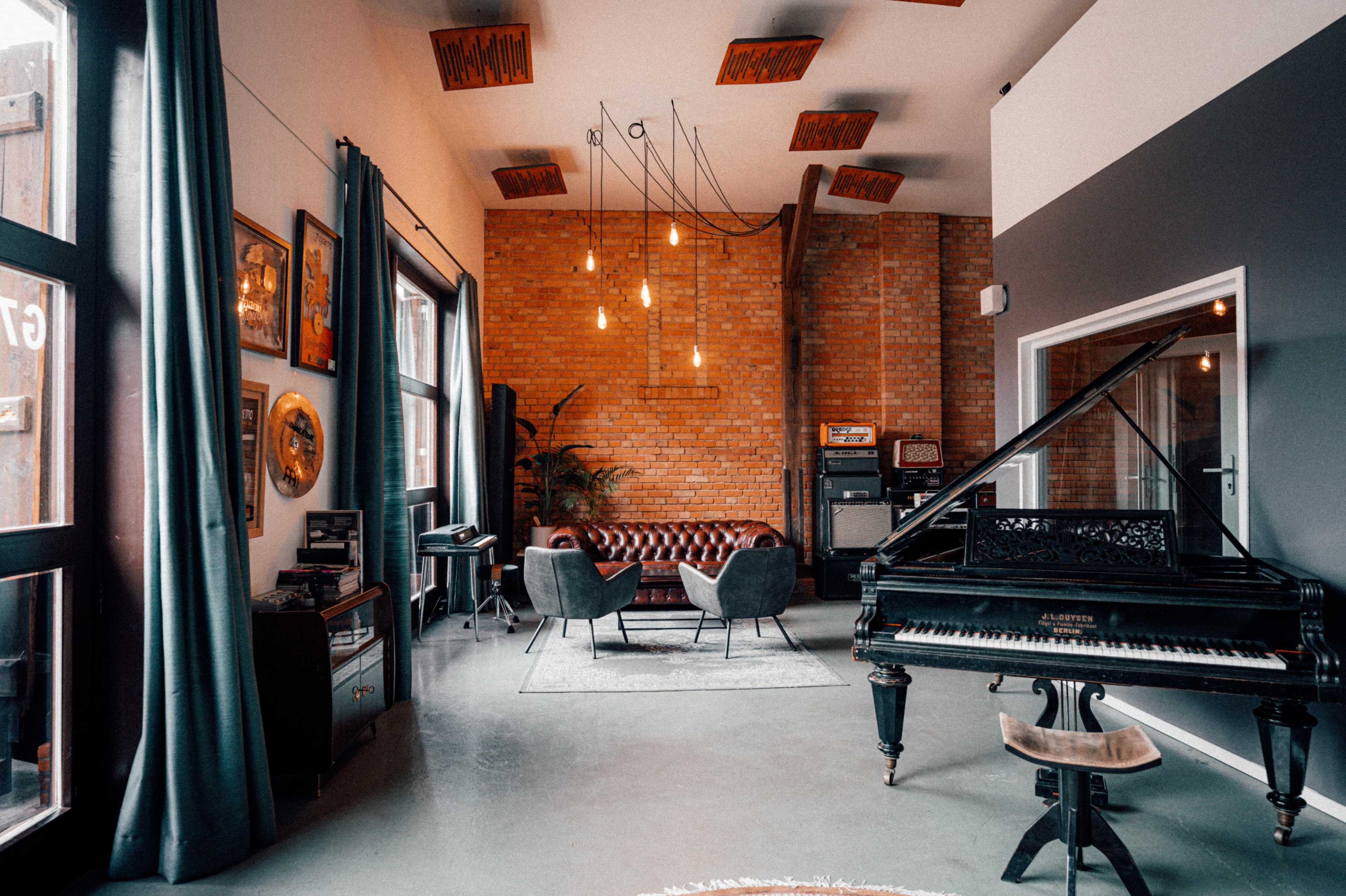 A stylish lounge area featuring a grand piano, comfortable seating, and exposed brick walls, illuminated by hanging pendant lights.