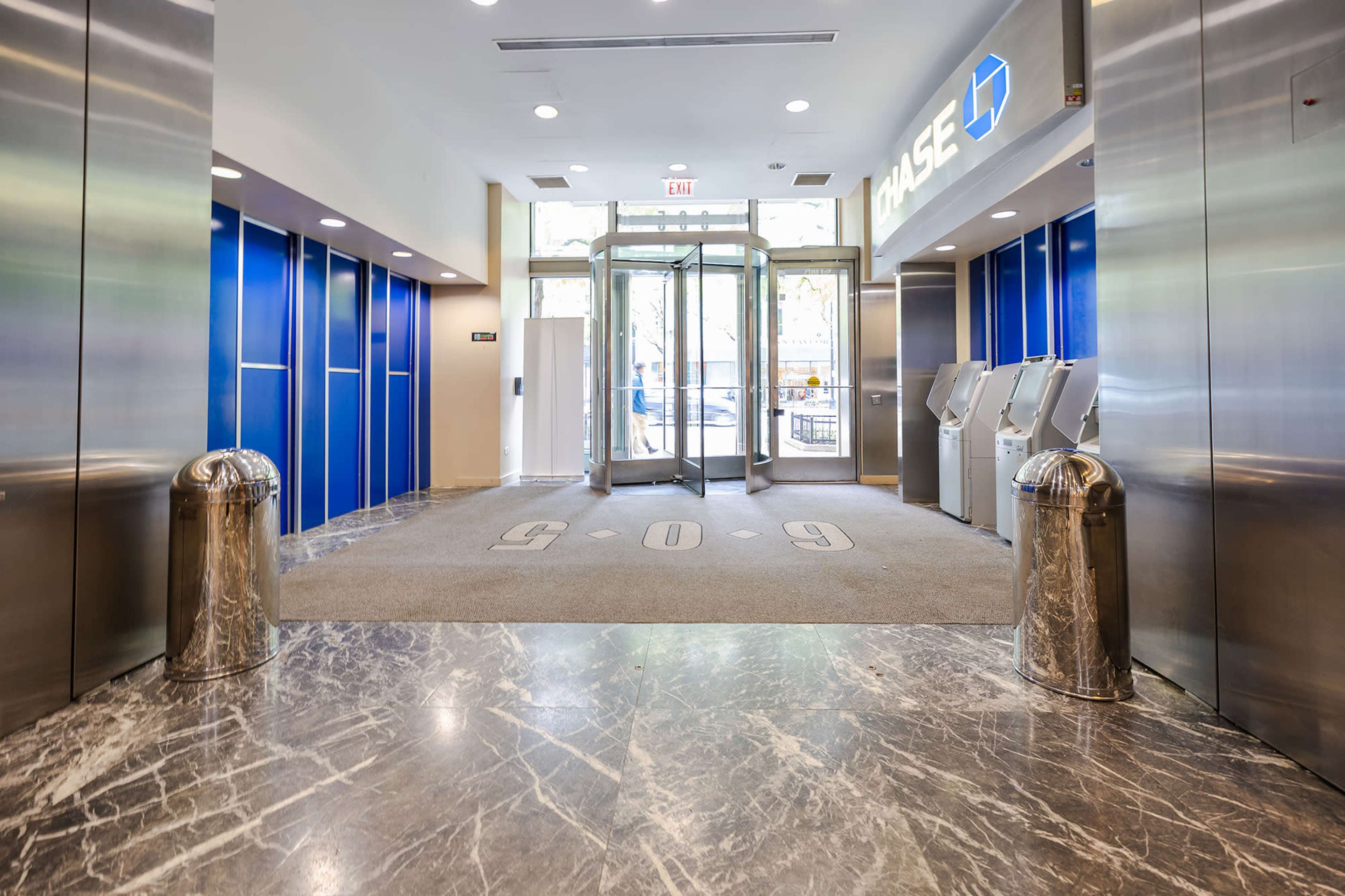 The image shows the entrance of a bank lobby featuring glass revolving doors and self-service kiosks on either side.