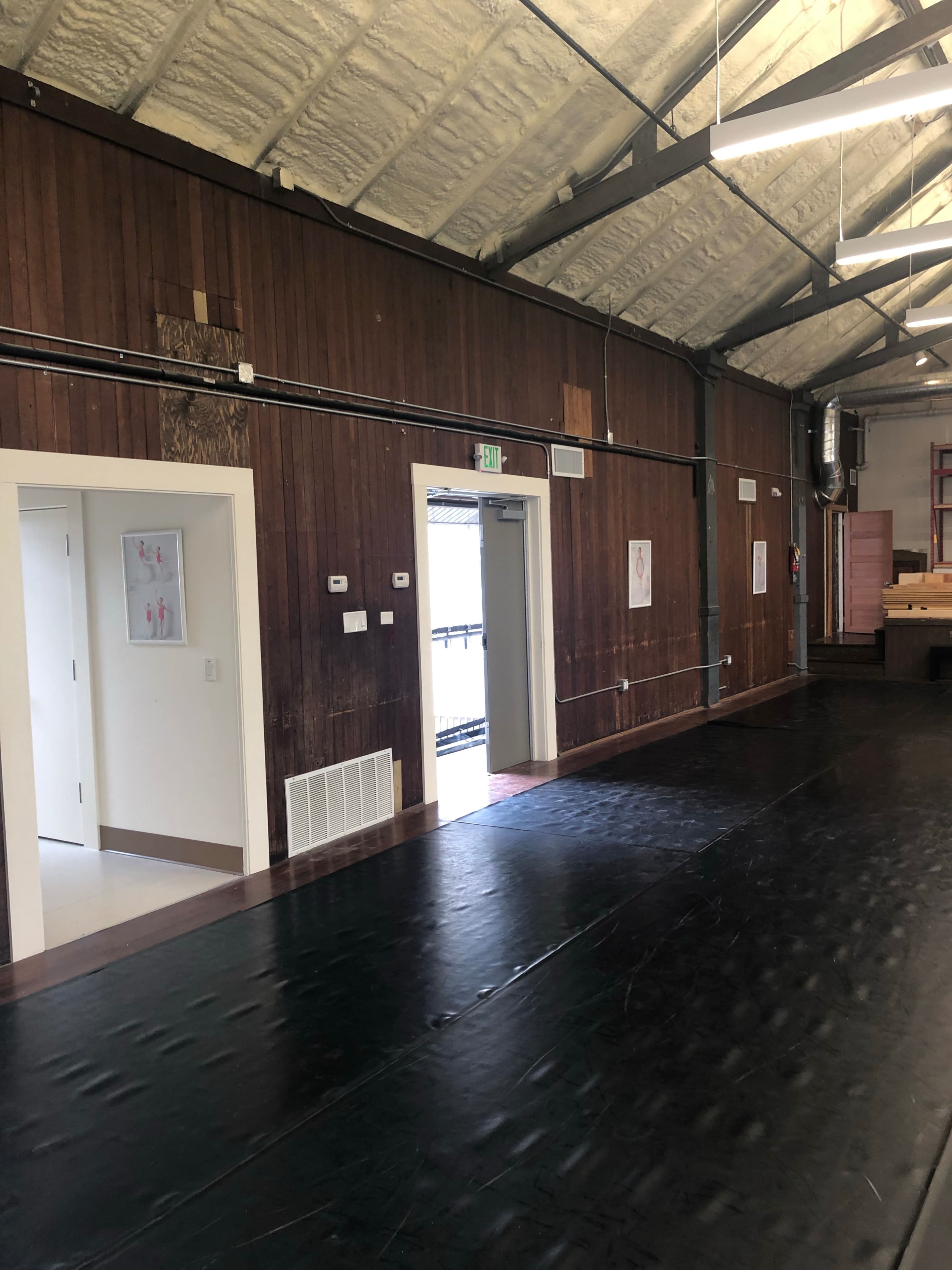 The image shows an interior space with wooden walls, a black flooring surface, and two doorways leading to adjacent rooms.