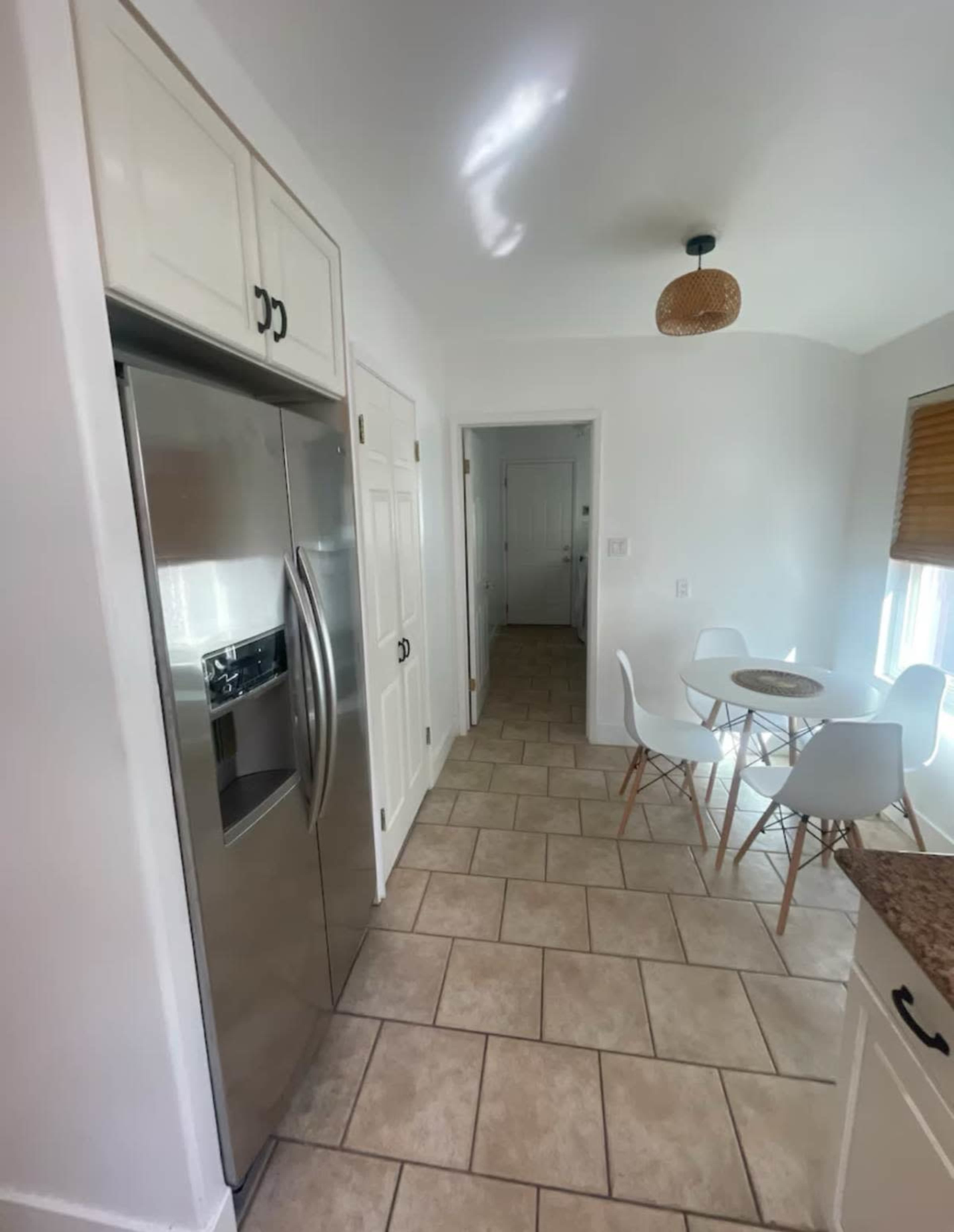 A kitchen space features a stainless steel refrigerator, light-colored cabinets, and a small dining area with a round table and white chairs.