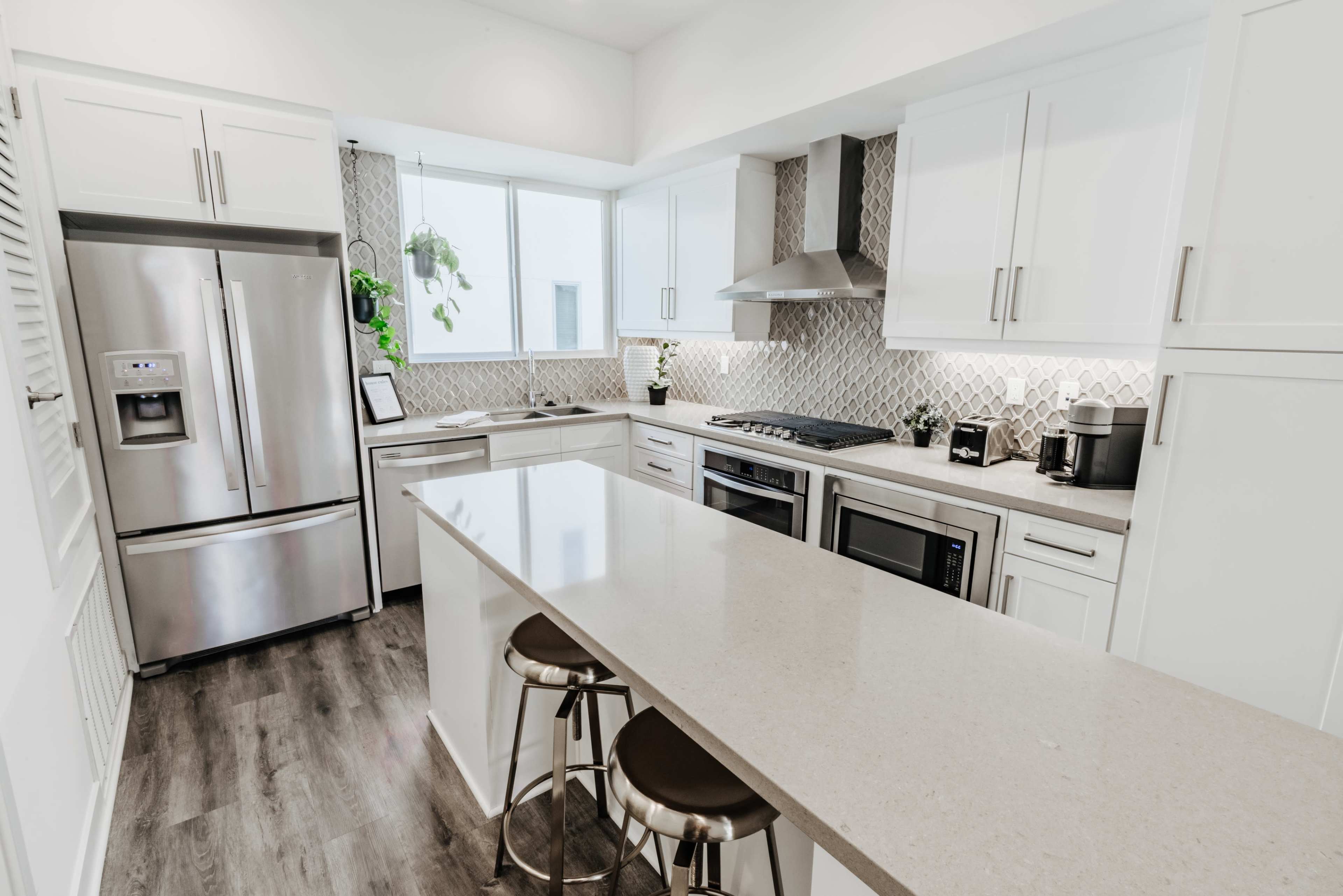 The image shows a modern kitchen featuring white cabinetry, stainless steel appliances, and a large island with bar stools.
