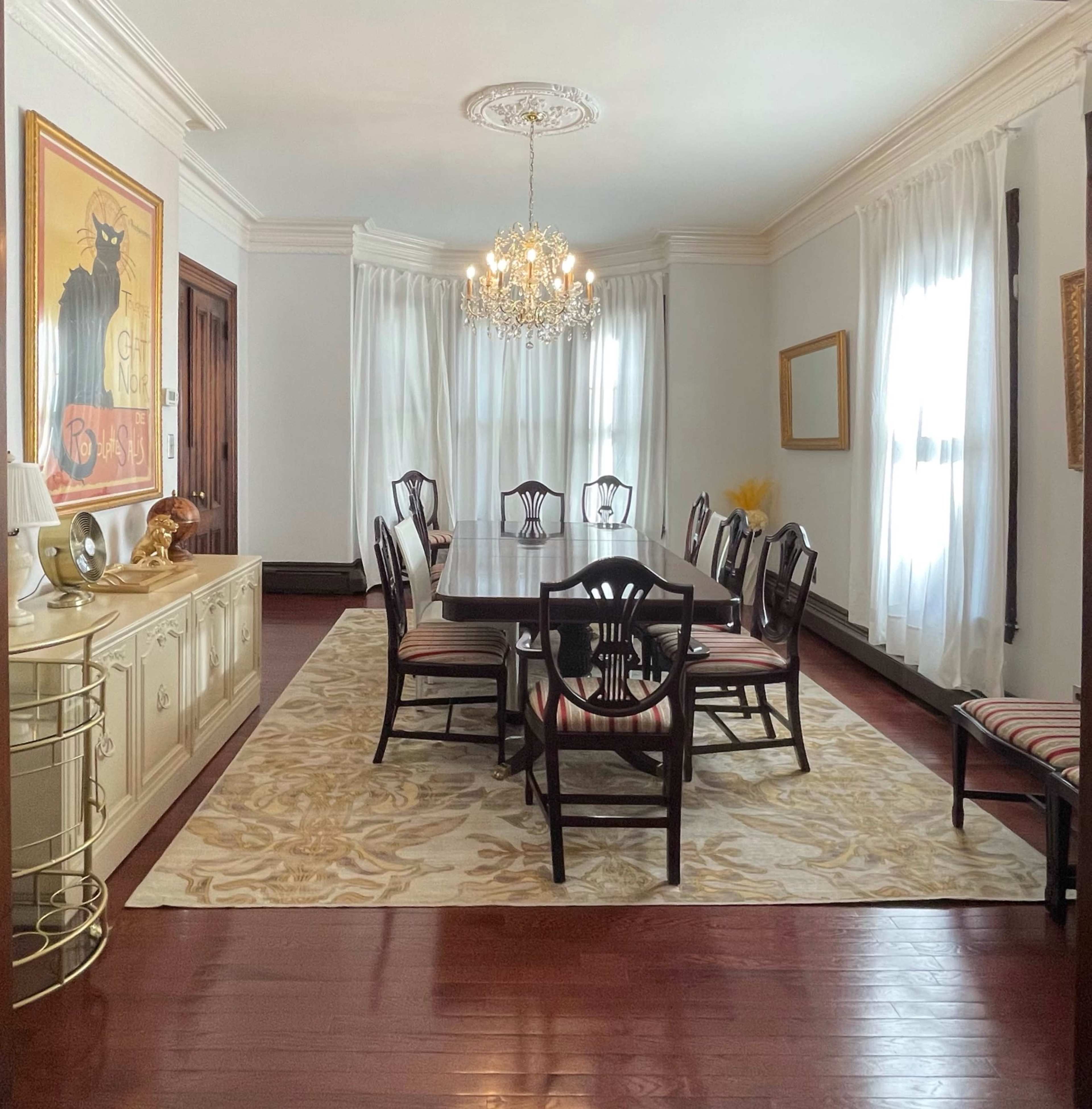 A dining room with a large rectangular table surrounded by chairs, a chandelier hanging from the ceiling, and decorative artwork on the walls.