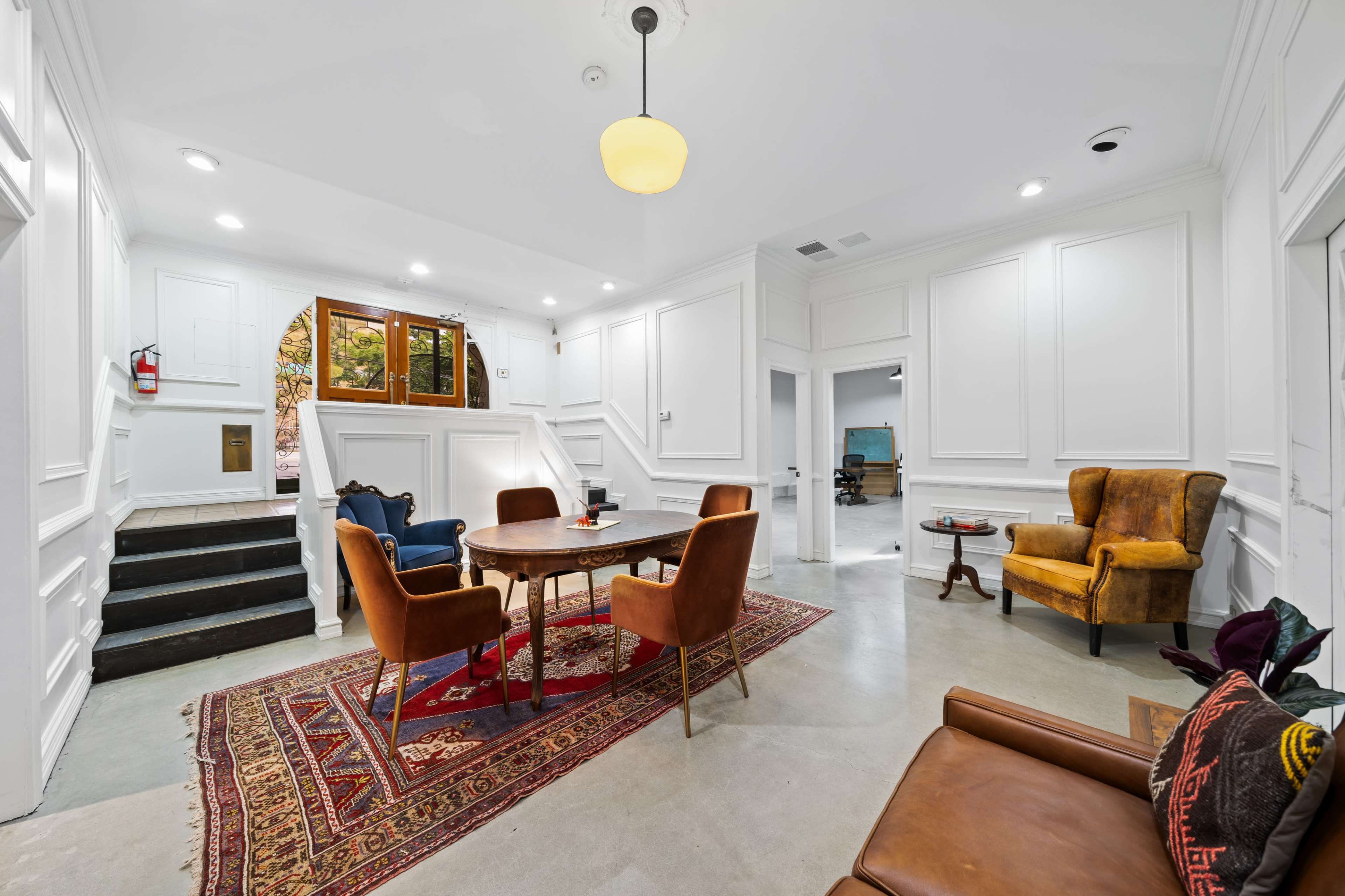 The image shows a well-lit entryway with a seating area that includes a round table and four chairs, flanked by a set of stairs leading to another level.