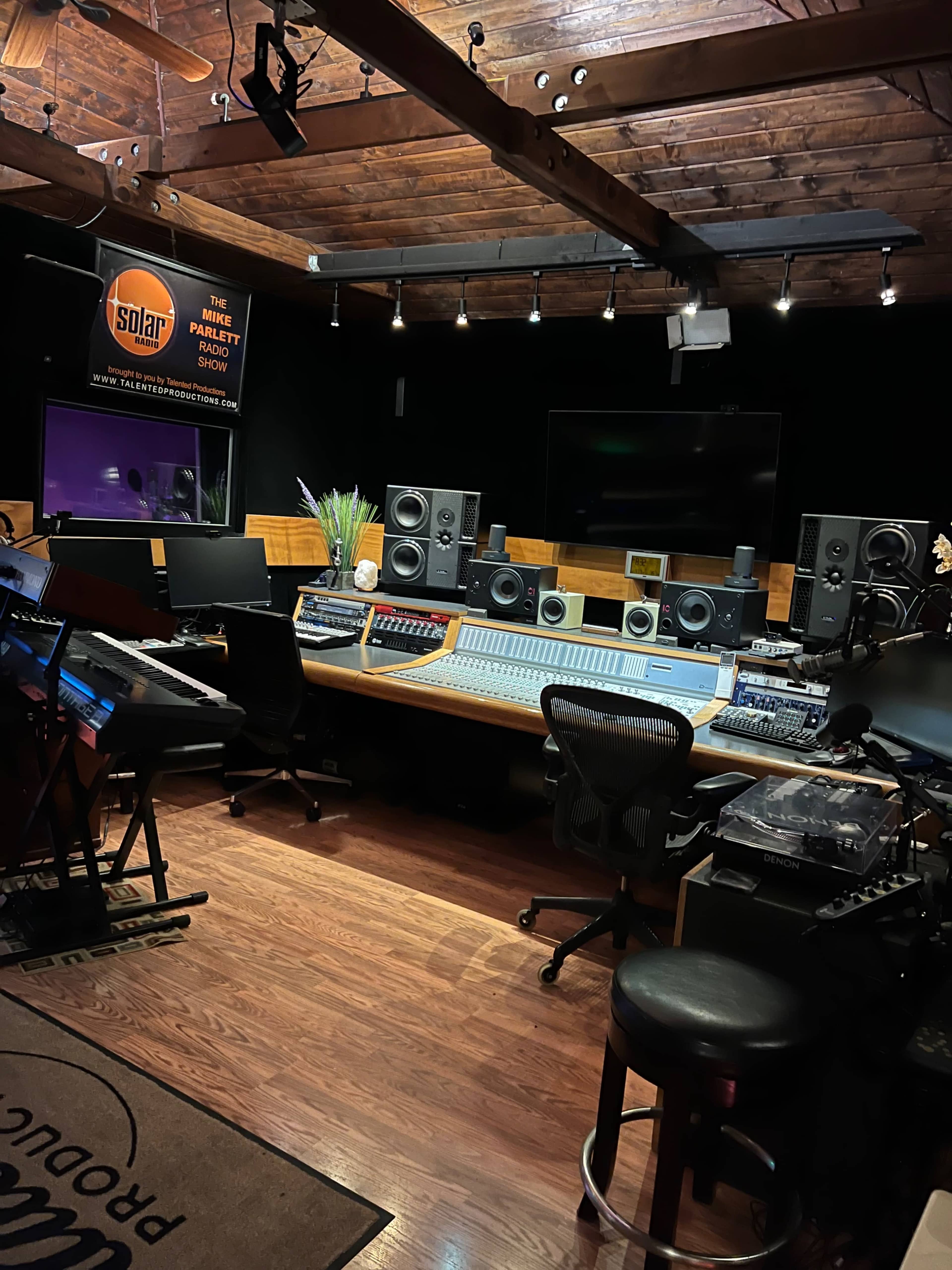 The image shows a music studio with a large mixing console, speakers, and various instruments neatly arranged in a well-lit space.