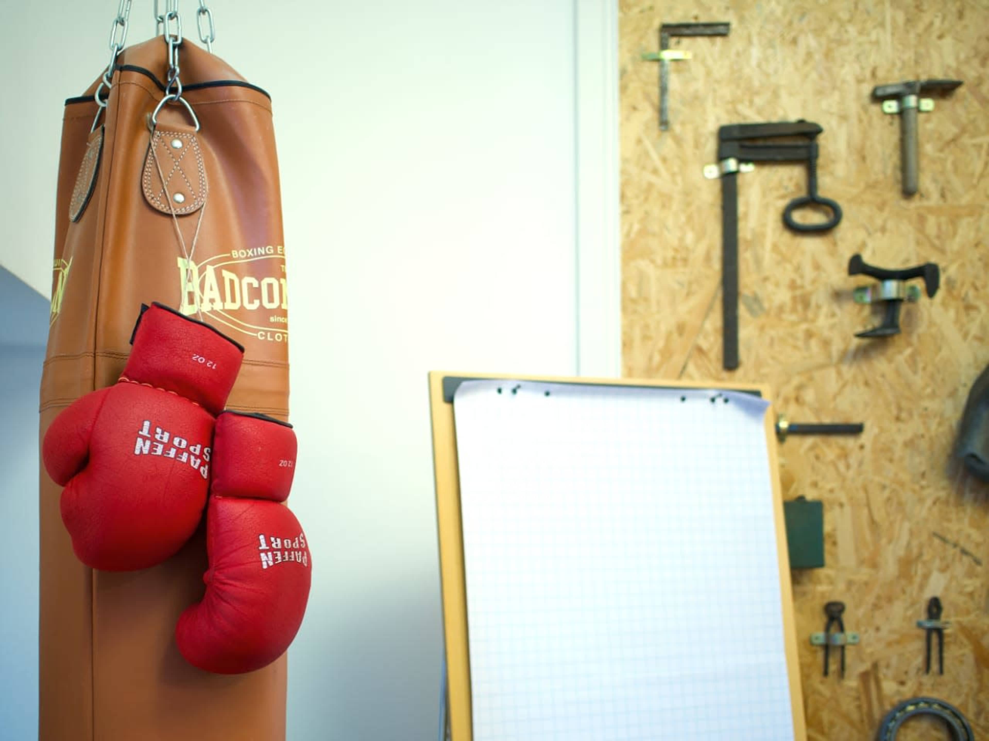 A brown punching bag hangs next to a wall adorned with various tools and a flip chart.