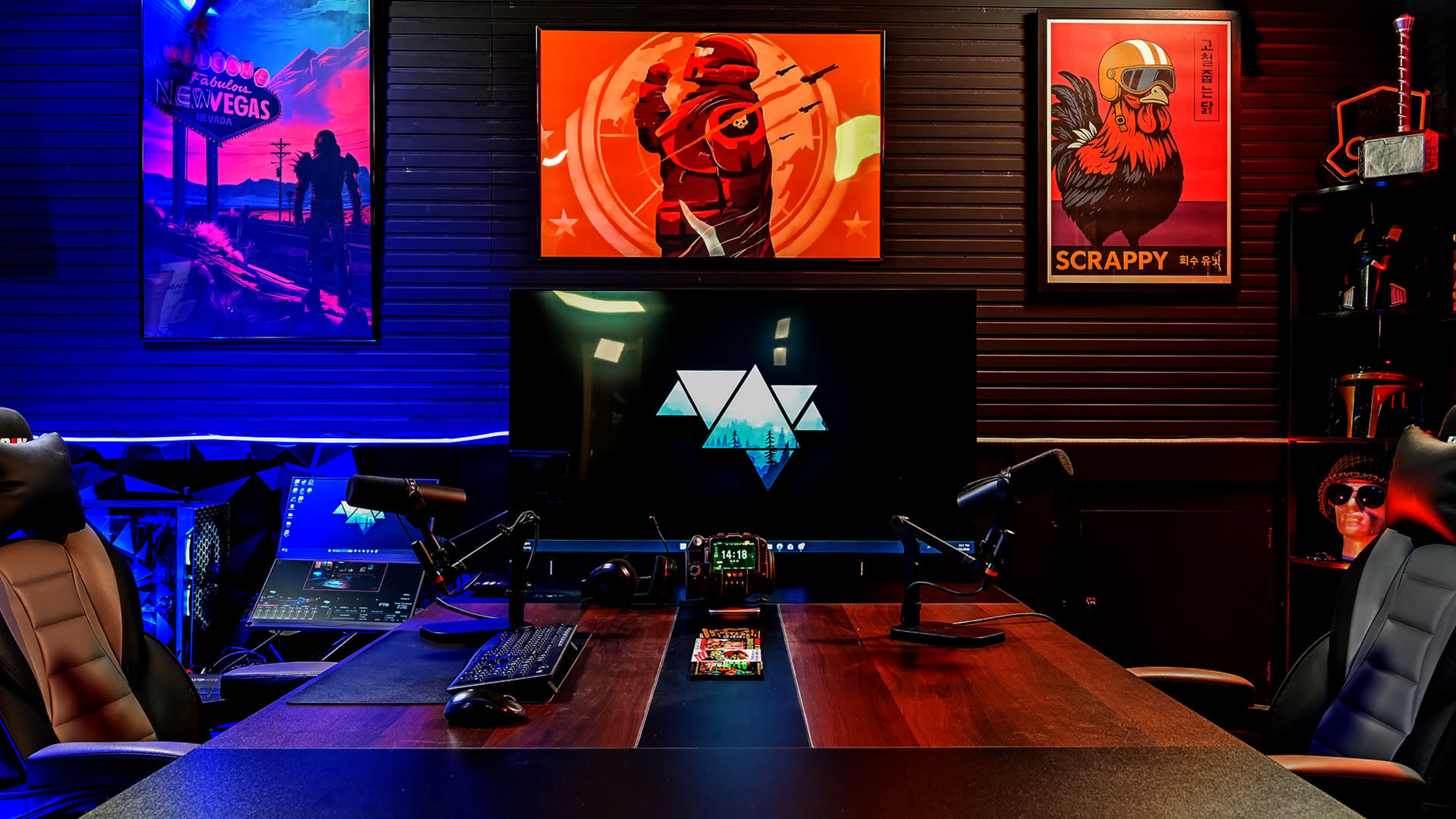 The image shows a modern gaming or media setup with two chairs, a large screen displaying a logo, and colorful artwork on the walls.