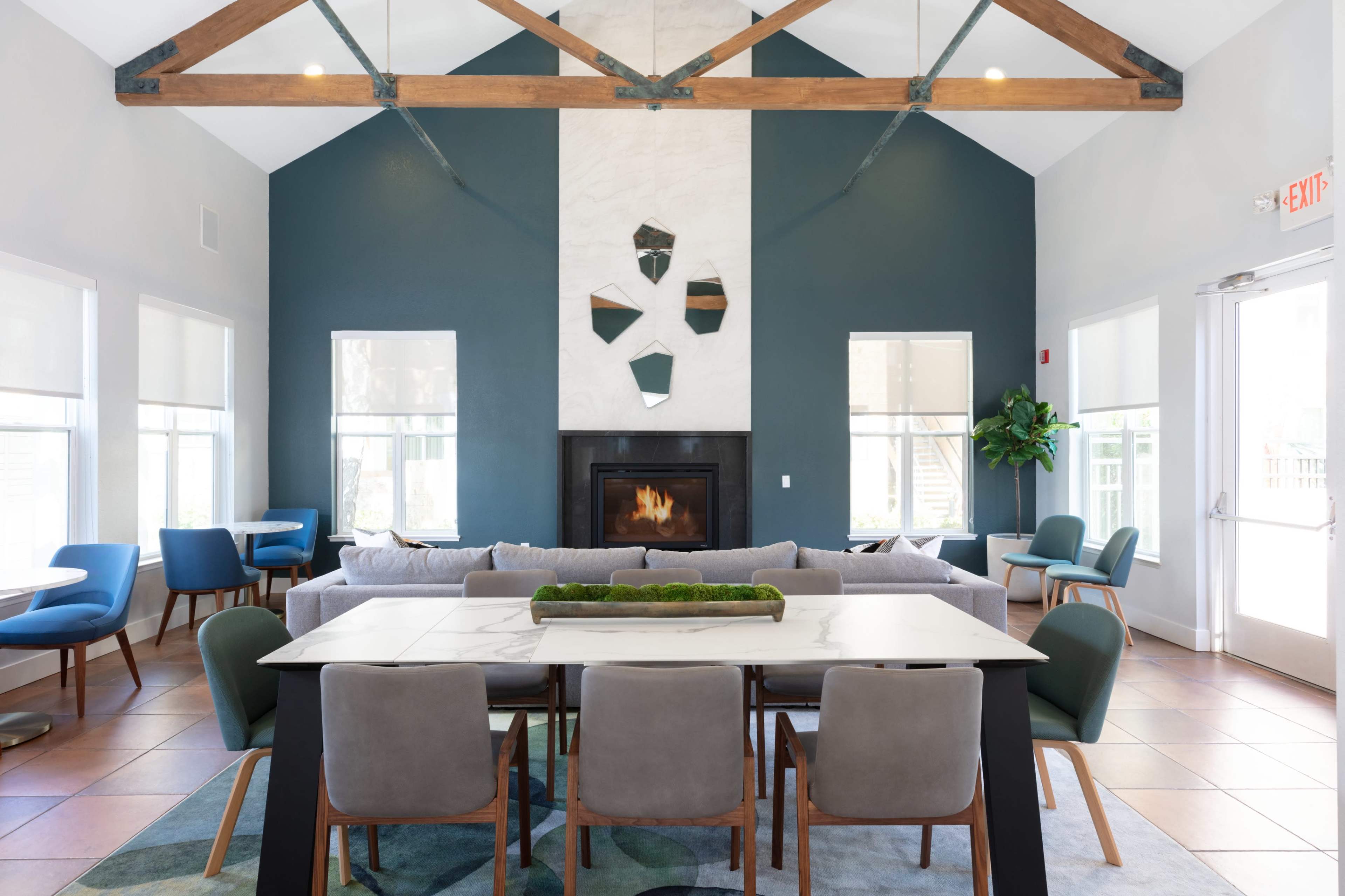 The image shows a modern lounge area with a fireplace, large windows, a dining table, and various seating arrangements.