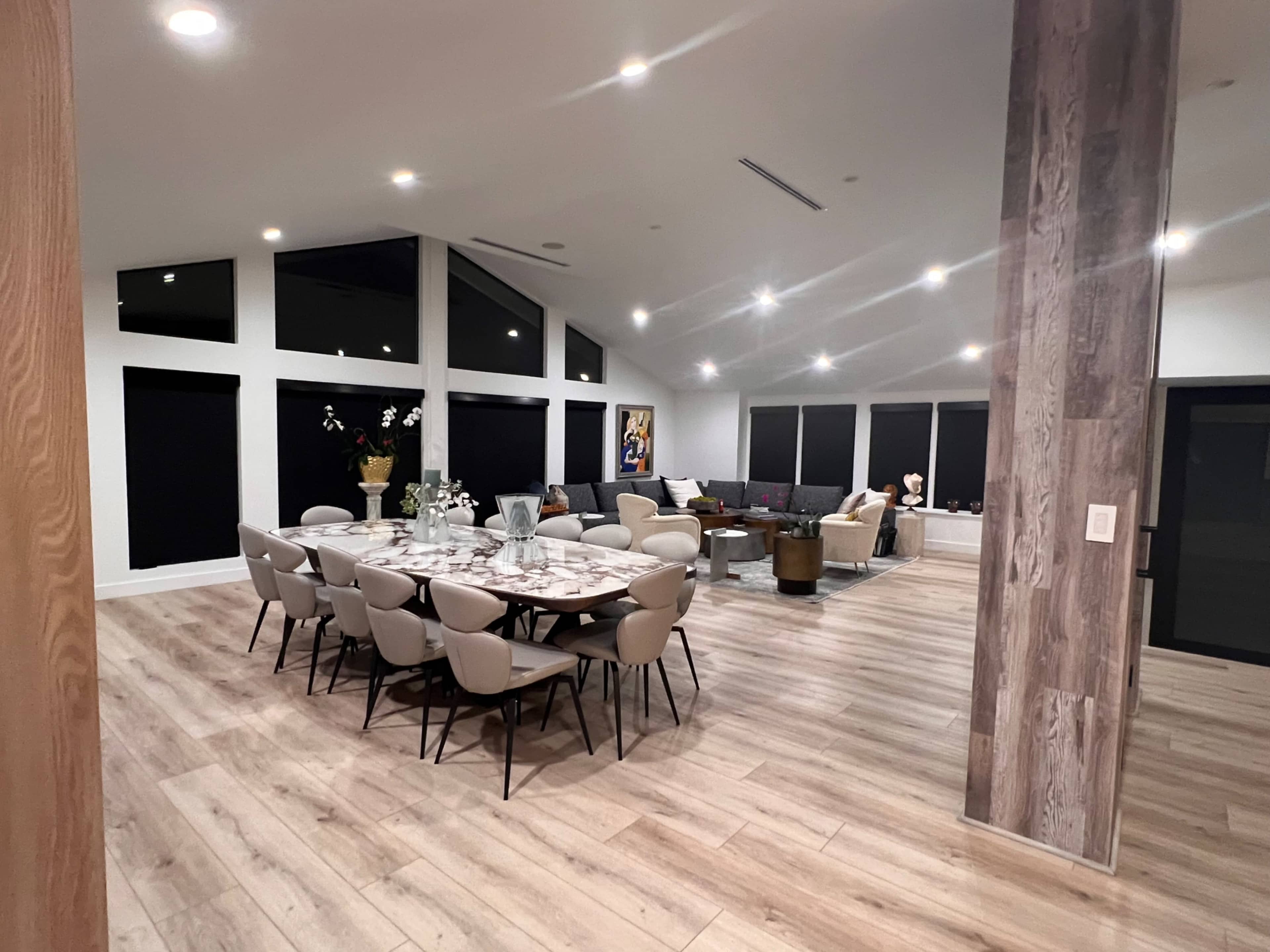 The image shows a spacious modern living and dining area with a large table set for dining, surrounded by stylish furniture and large windows.