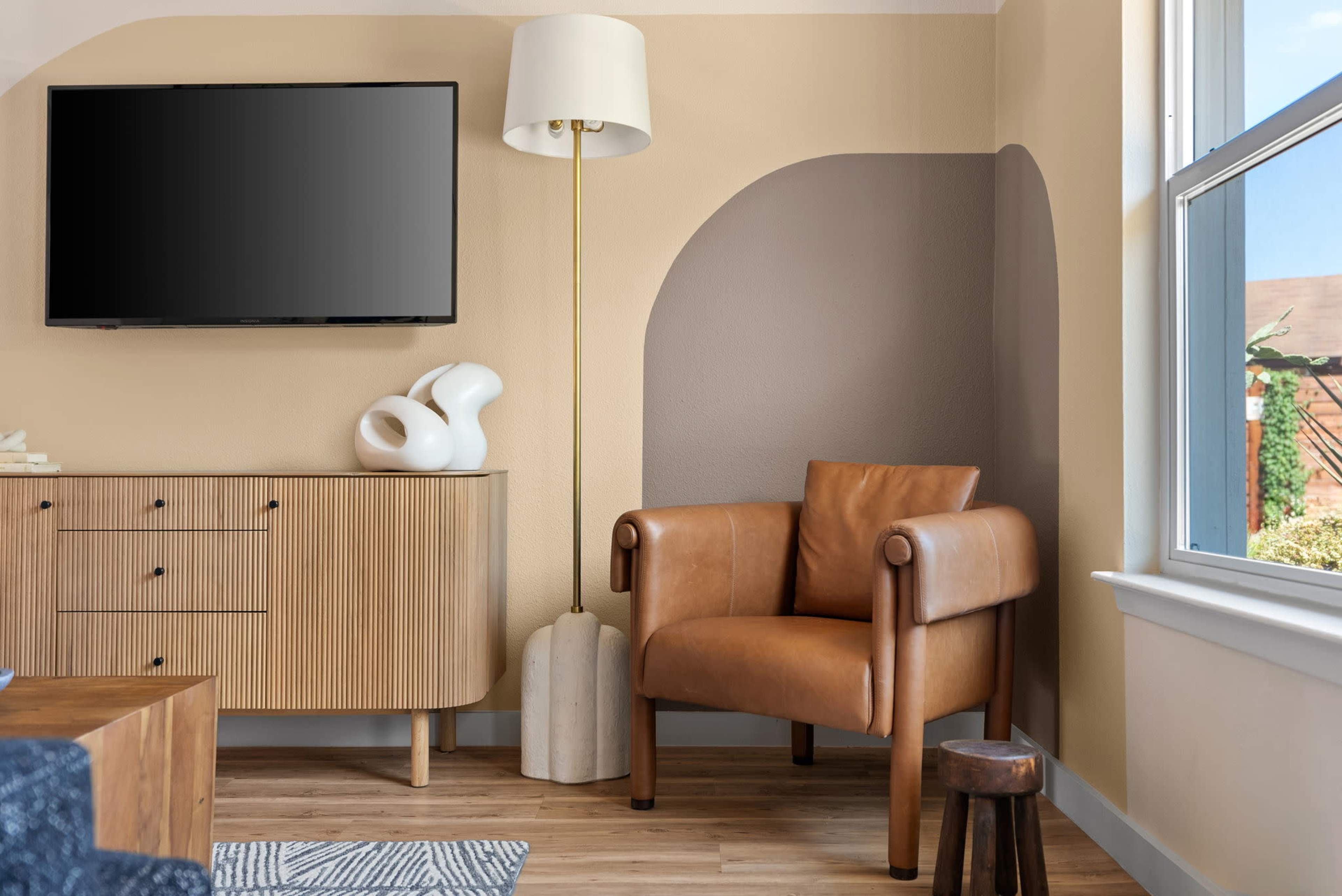 The image shows a neatly arranged living space featuring a modern television, a wooden sideboard, a stylish leather armchair, and a floor lamp.
