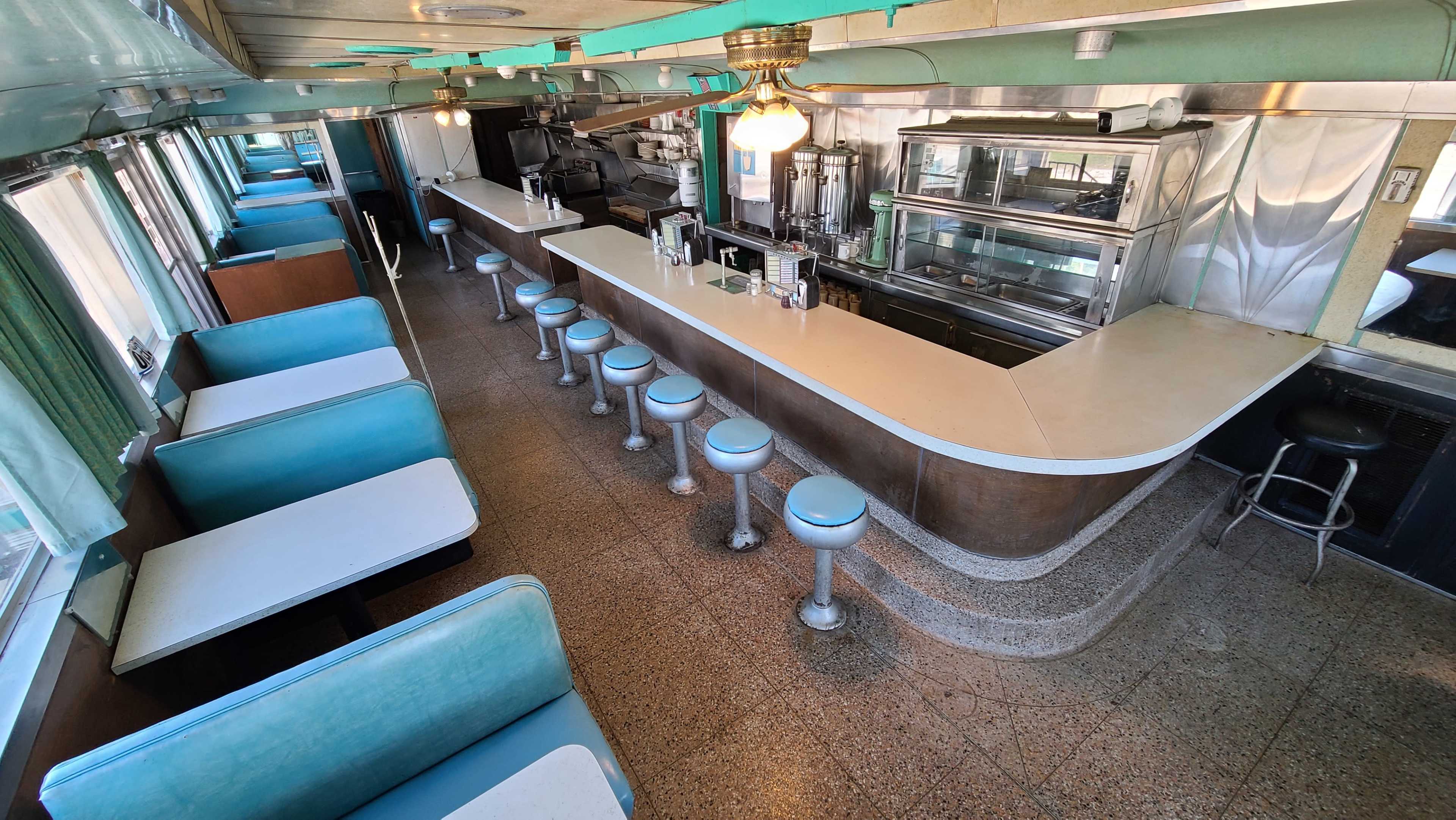 The interior of a vintage diner featuring a long counter with stools and turquoise seating booths.