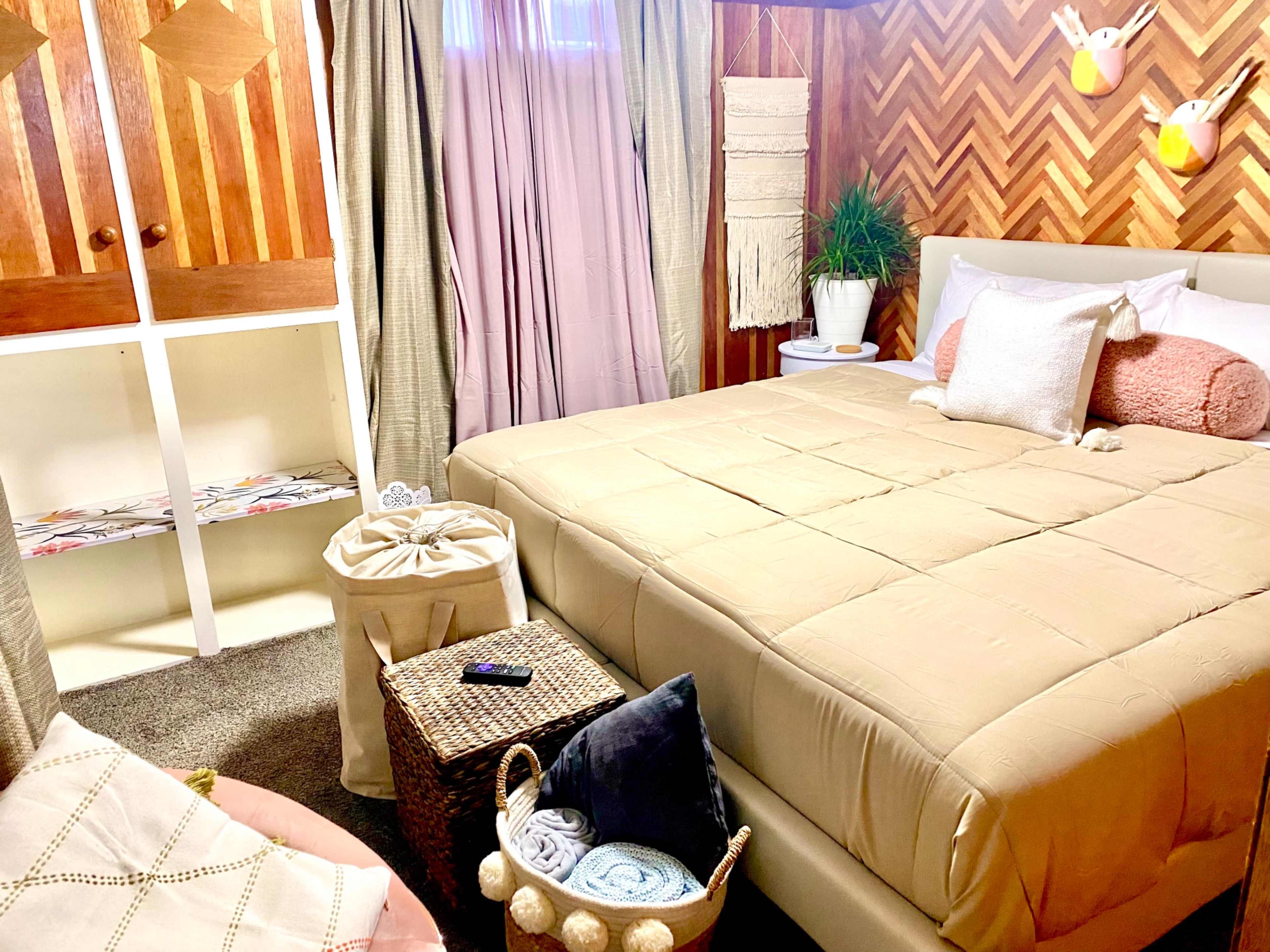 A cozy bedroom with a neatly made bed, storage baskets, and decorative elements against a patterned wood wall.