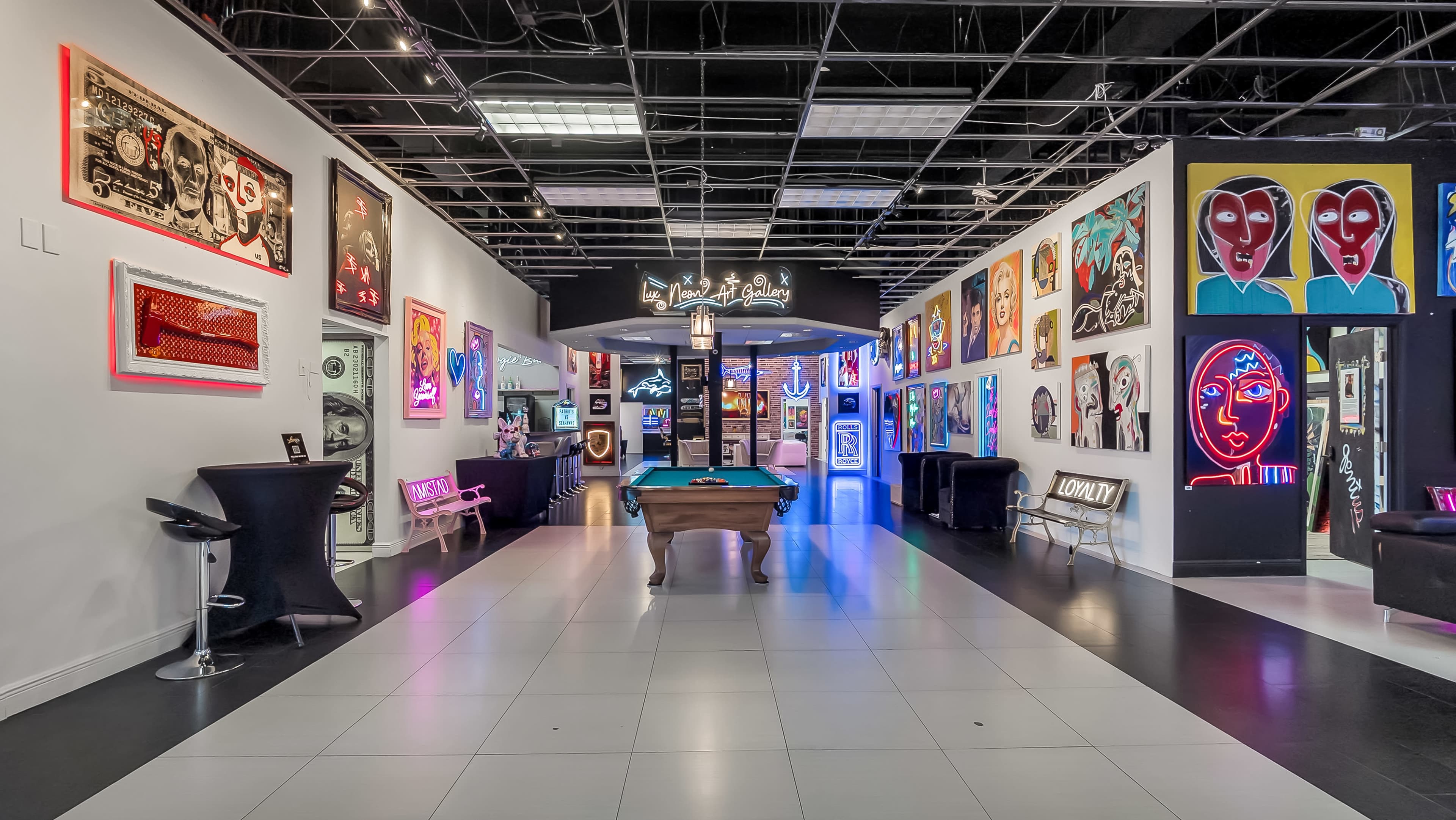 The image shows a modern art gallery with colorful artwork on the walls, a pool table in the center, and a large sign reading "Live Art" above the entrance to a lounge area.