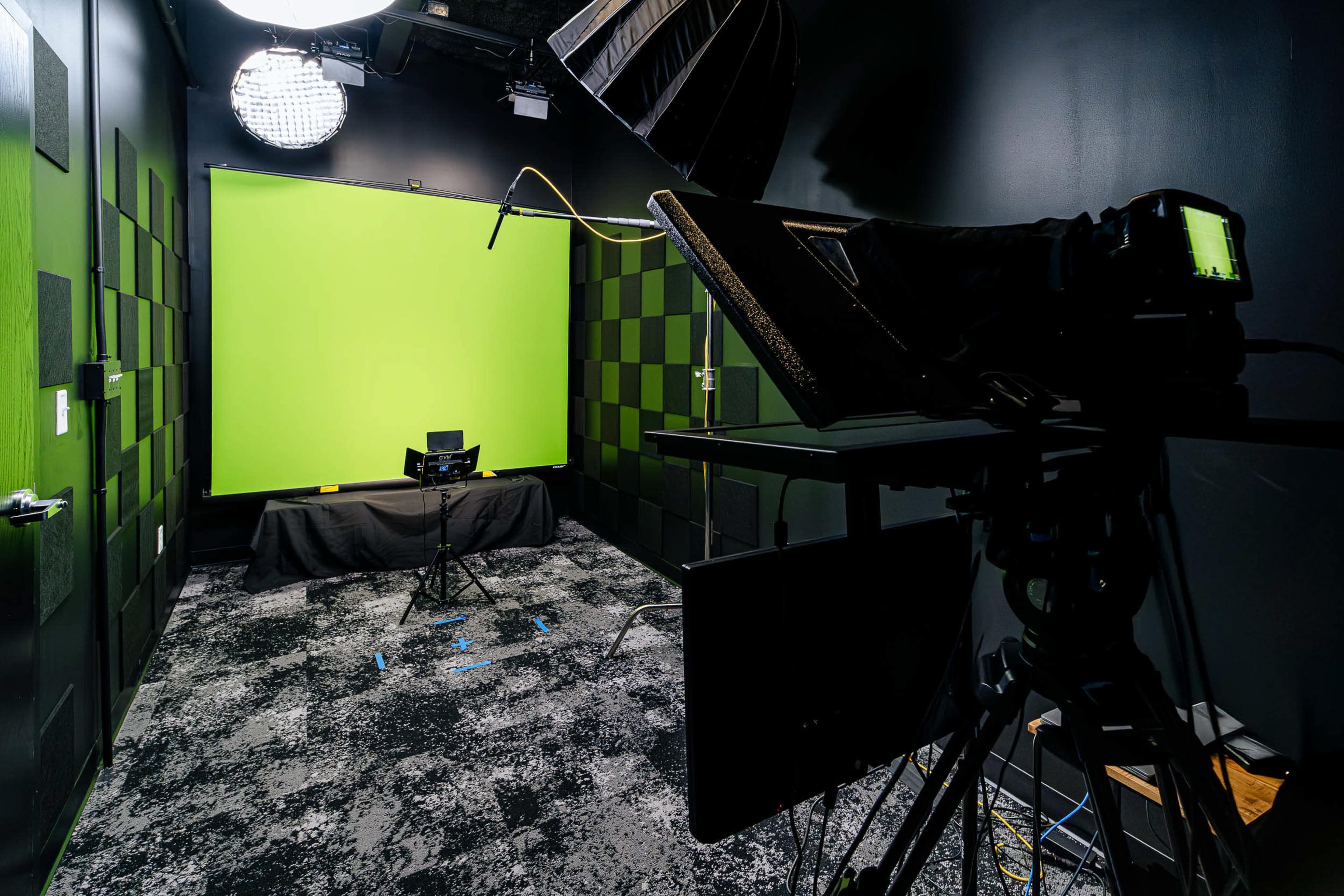 The image shows a studio setup with a green screen backdrop, cameras, lighting equipment, and a patterned black and green wall.