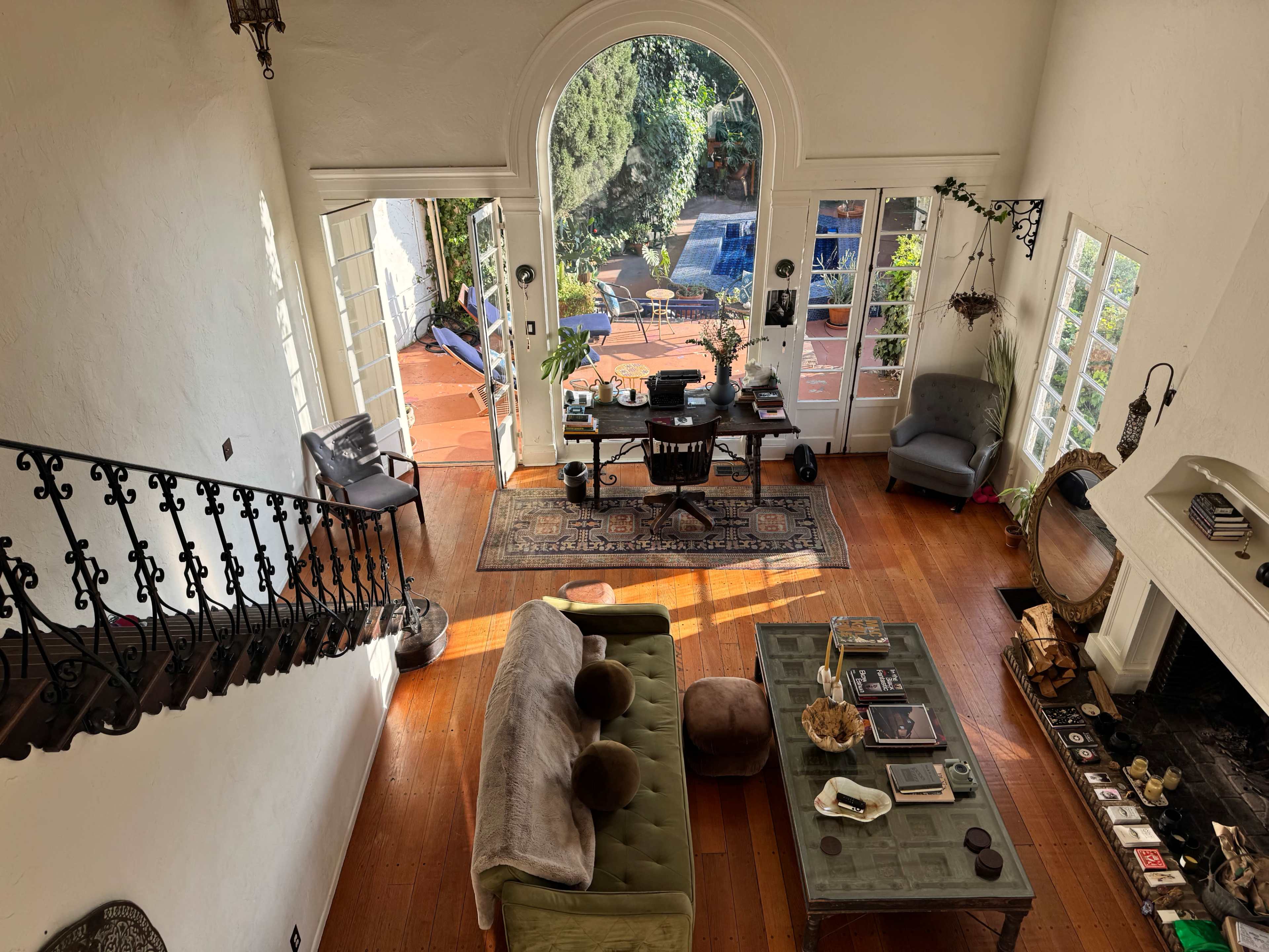 A spacious living room features a large green sofa, a coffee table with various items, and doors leading to an outdoor patio and pool area.