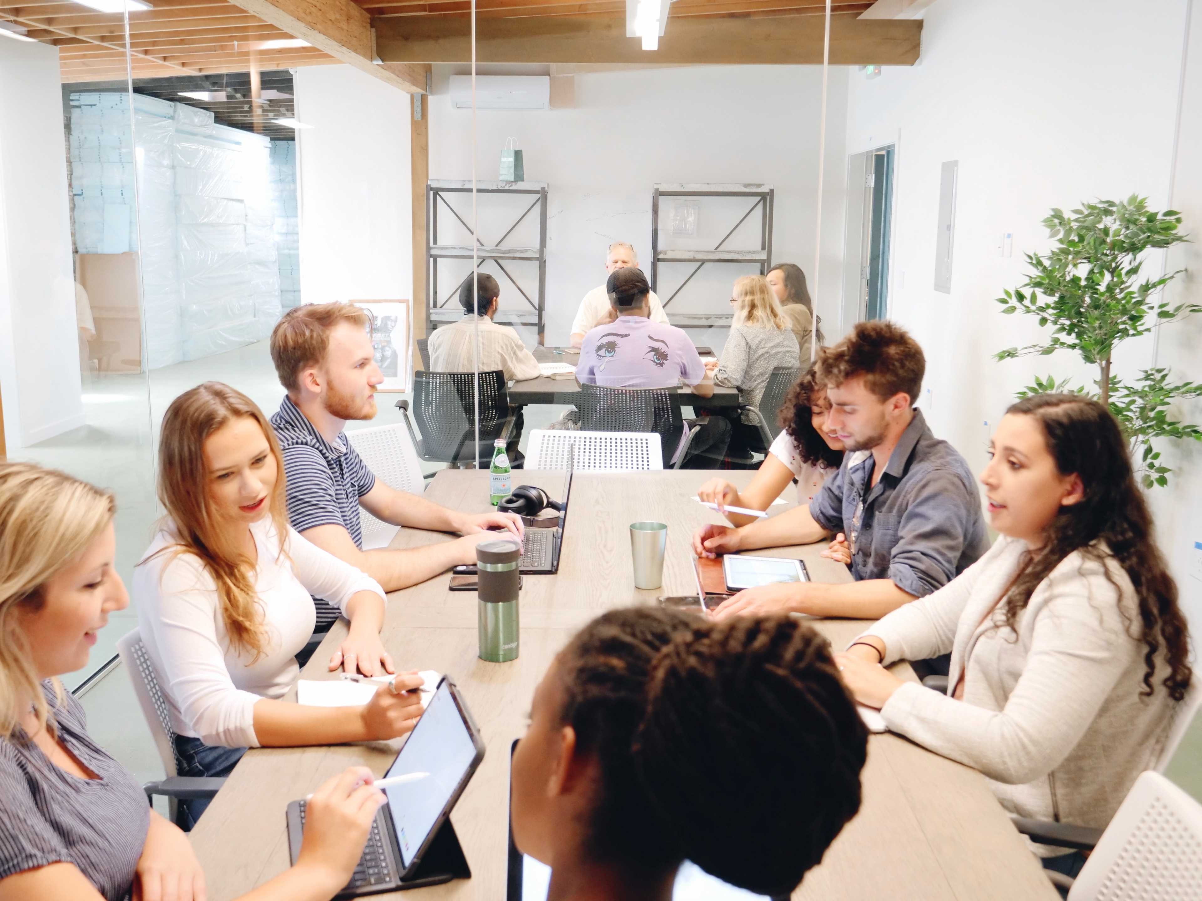 A group of people engages in a discussion around a long table in a modern conference room.