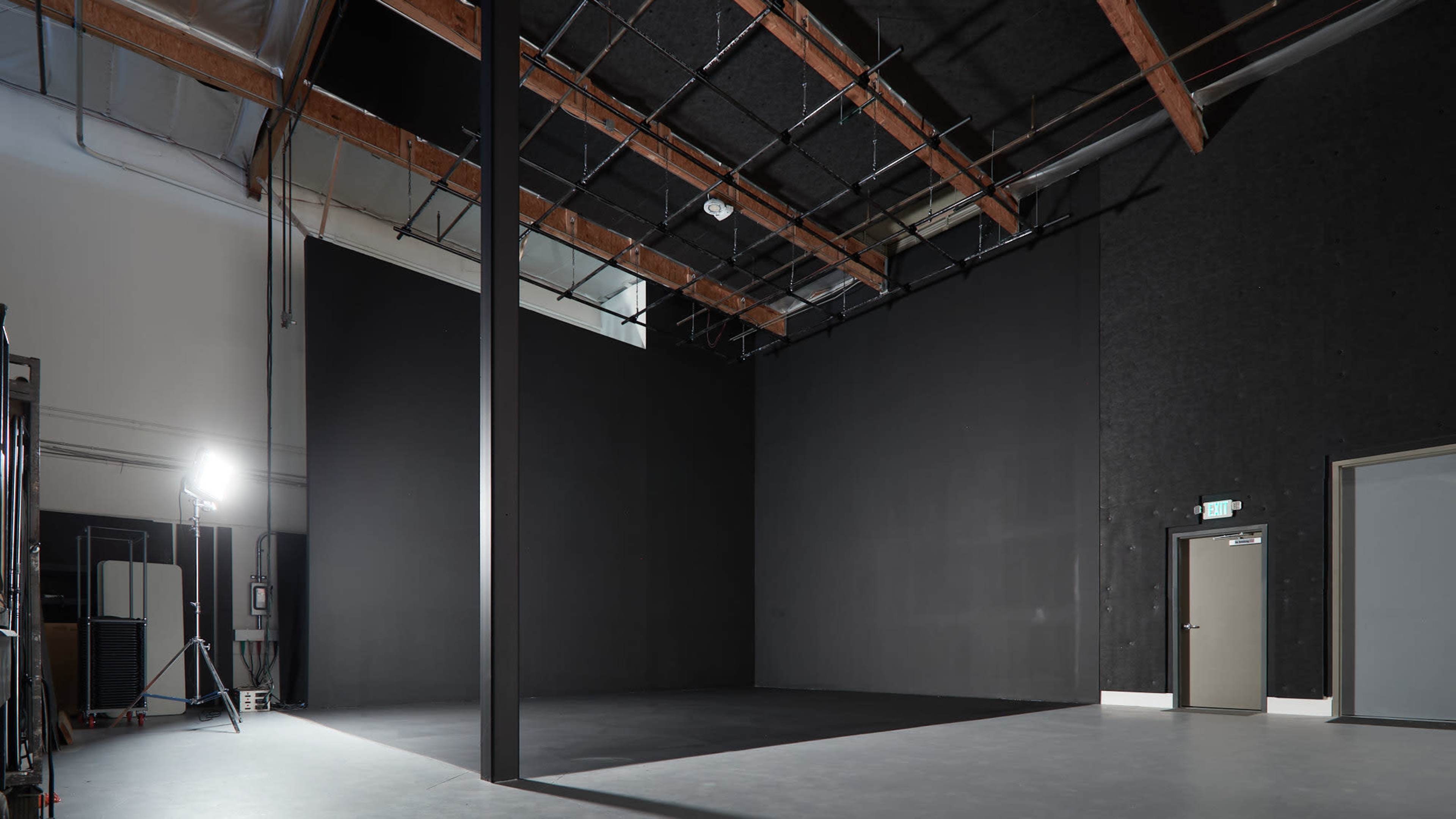 A large, empty studio space with dark walls, a high ceiling, and a single light source illuminating one corner.