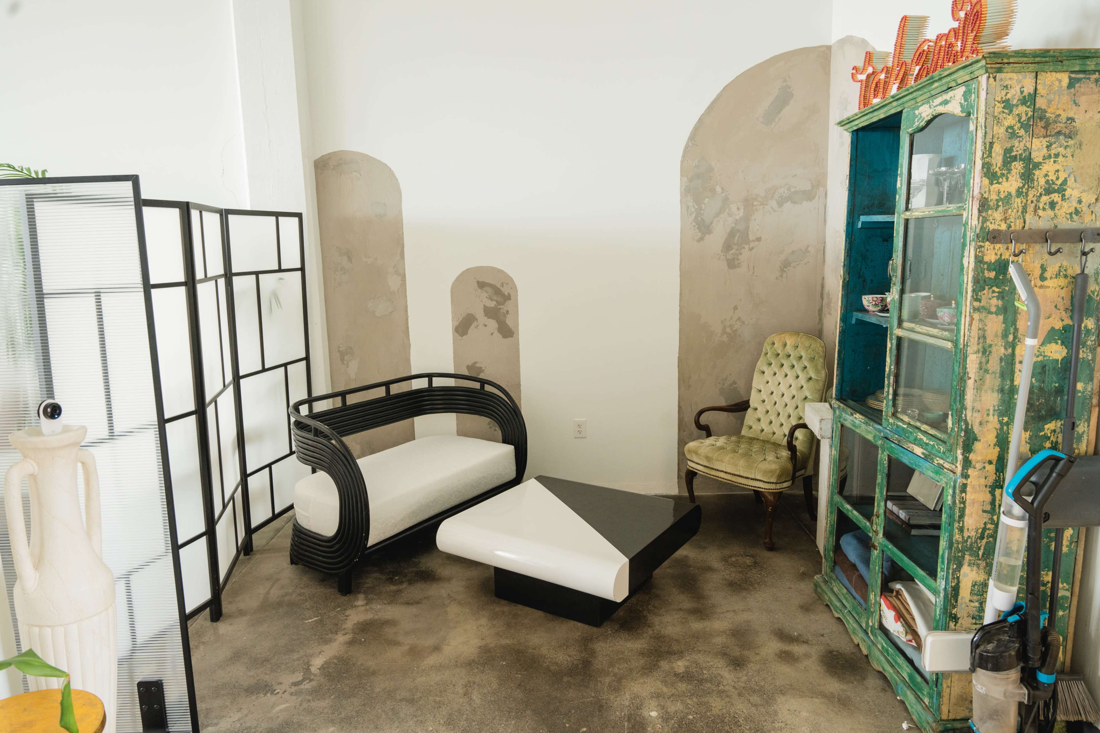 A small interior space featuring a black and white coffee table, a curved black sofa, a green vintage cabinet, and an ornate armchair against a textured wall.
