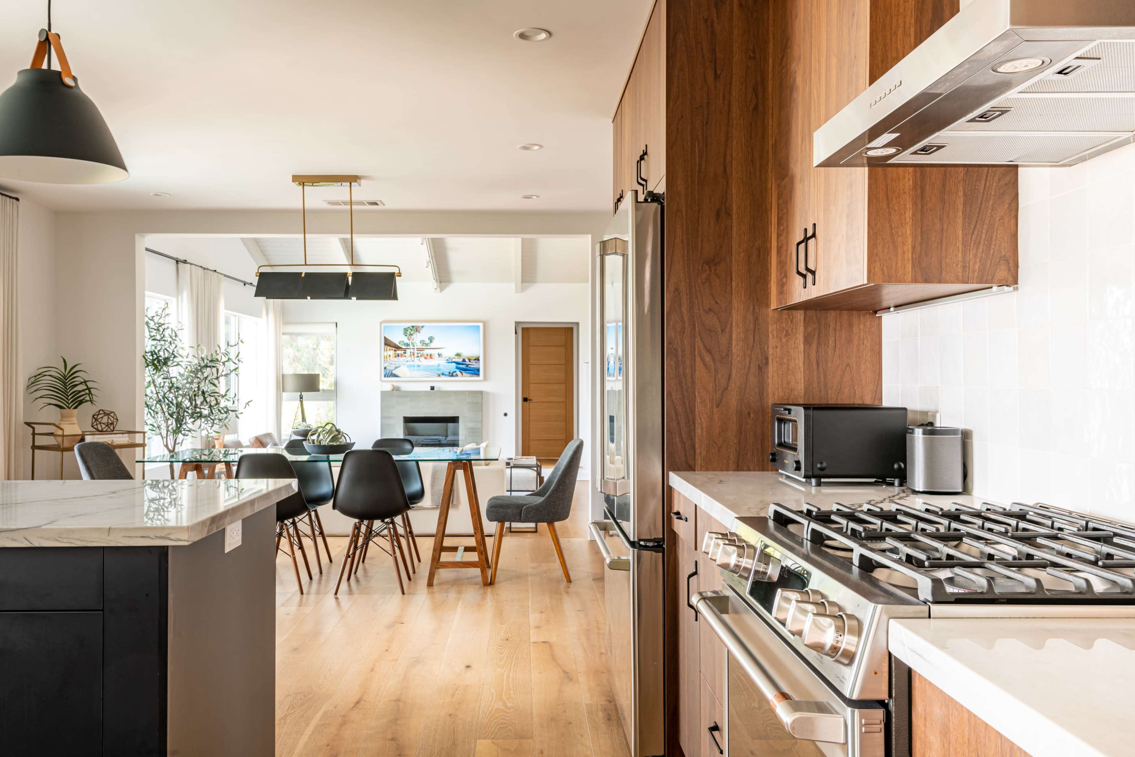 A modern kitchen with a gas stove and stainless steel appliances opens into a dining area featuring a wooden table and black chairs.